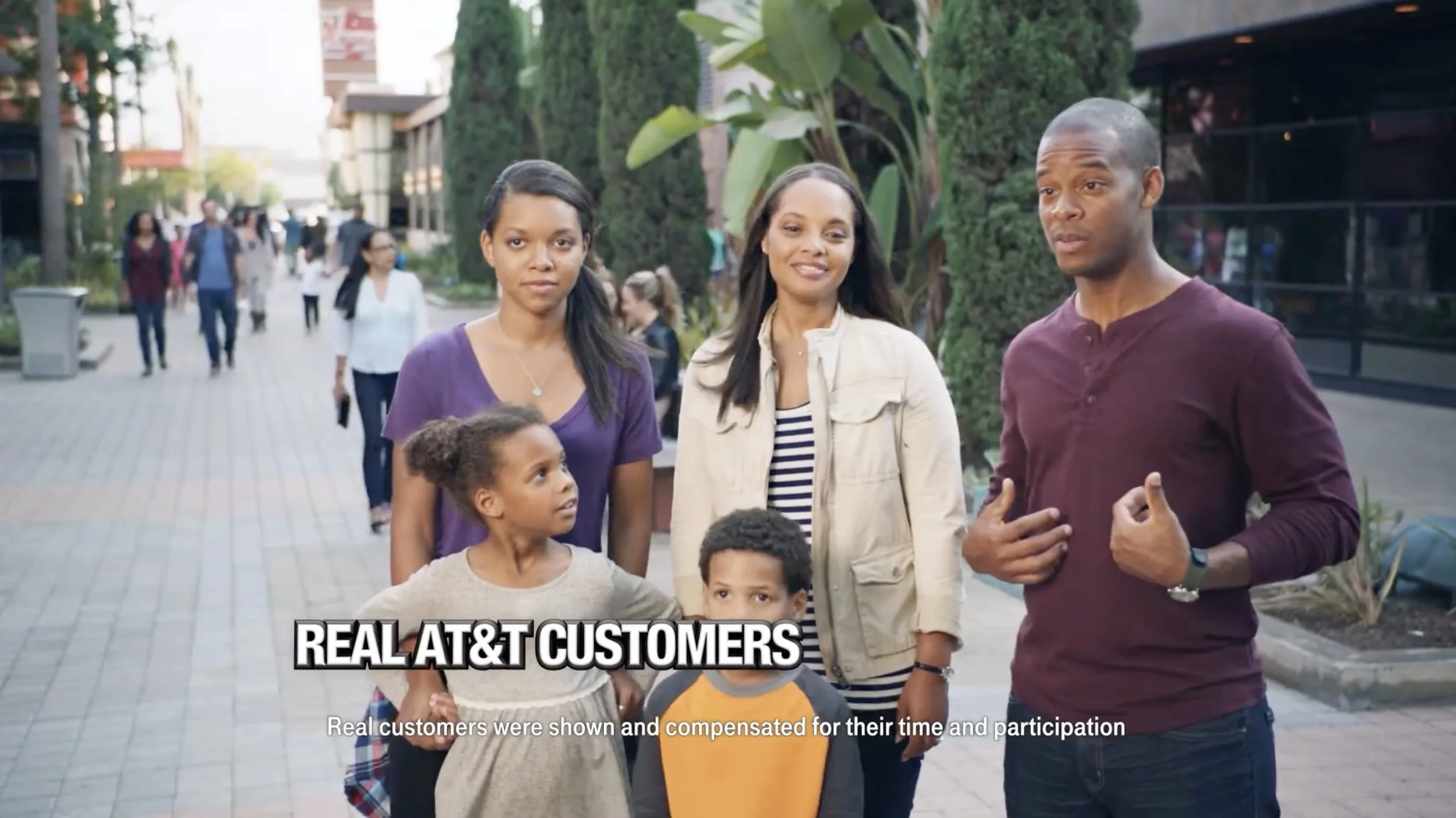 T-mobile TV commercial. A mom and dad, and two children on a city sidewalk, with pedestrians and storefronts in the background.