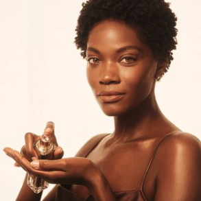 Black model with short curly hair holding a 'JLo Beauty' bottle in her hand