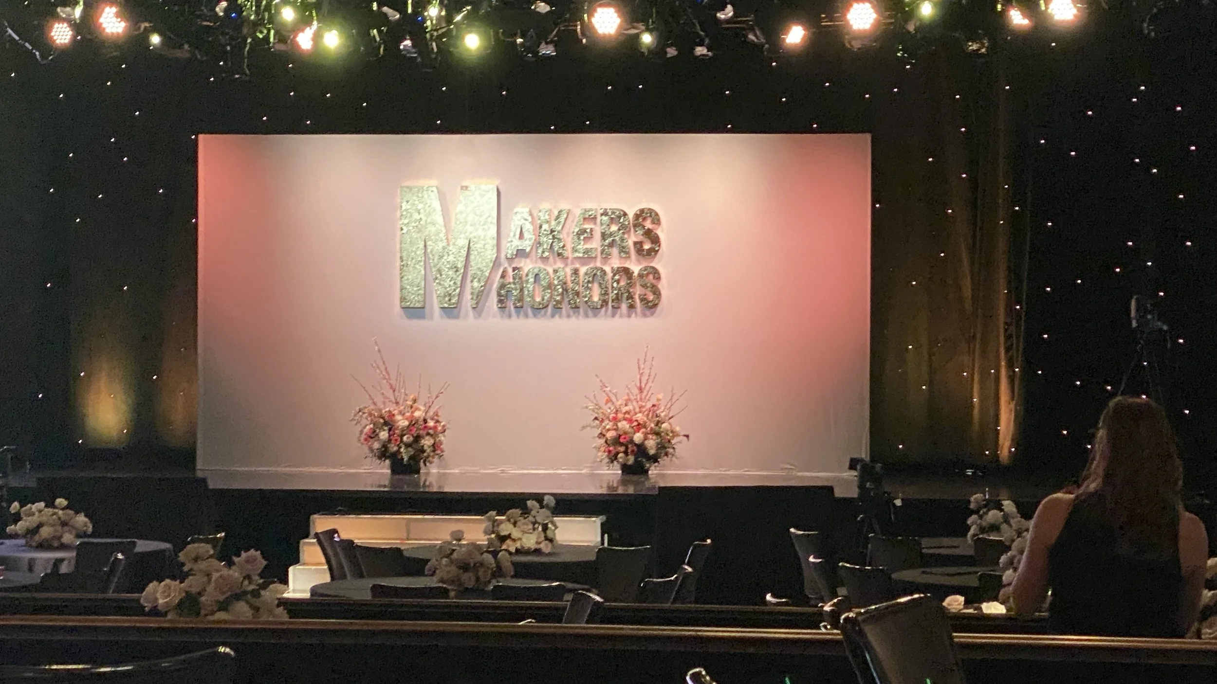 An event stage with the words 'Makers & Honors' on a large screen, decorated with floral arrangements and a woman sitting in the audience. For Yahoo Makers conference.
