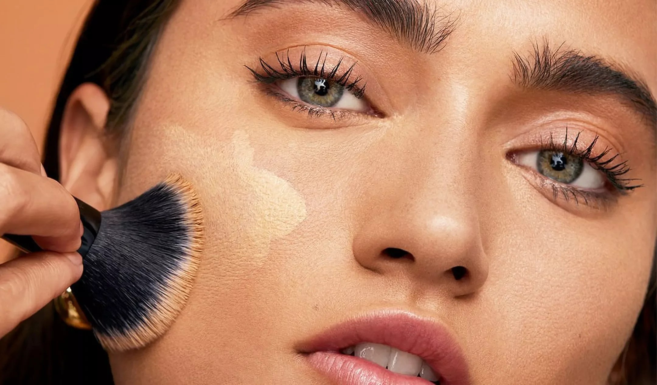 Close-up of a woman applying foundation makeup with a brush on her cheek.