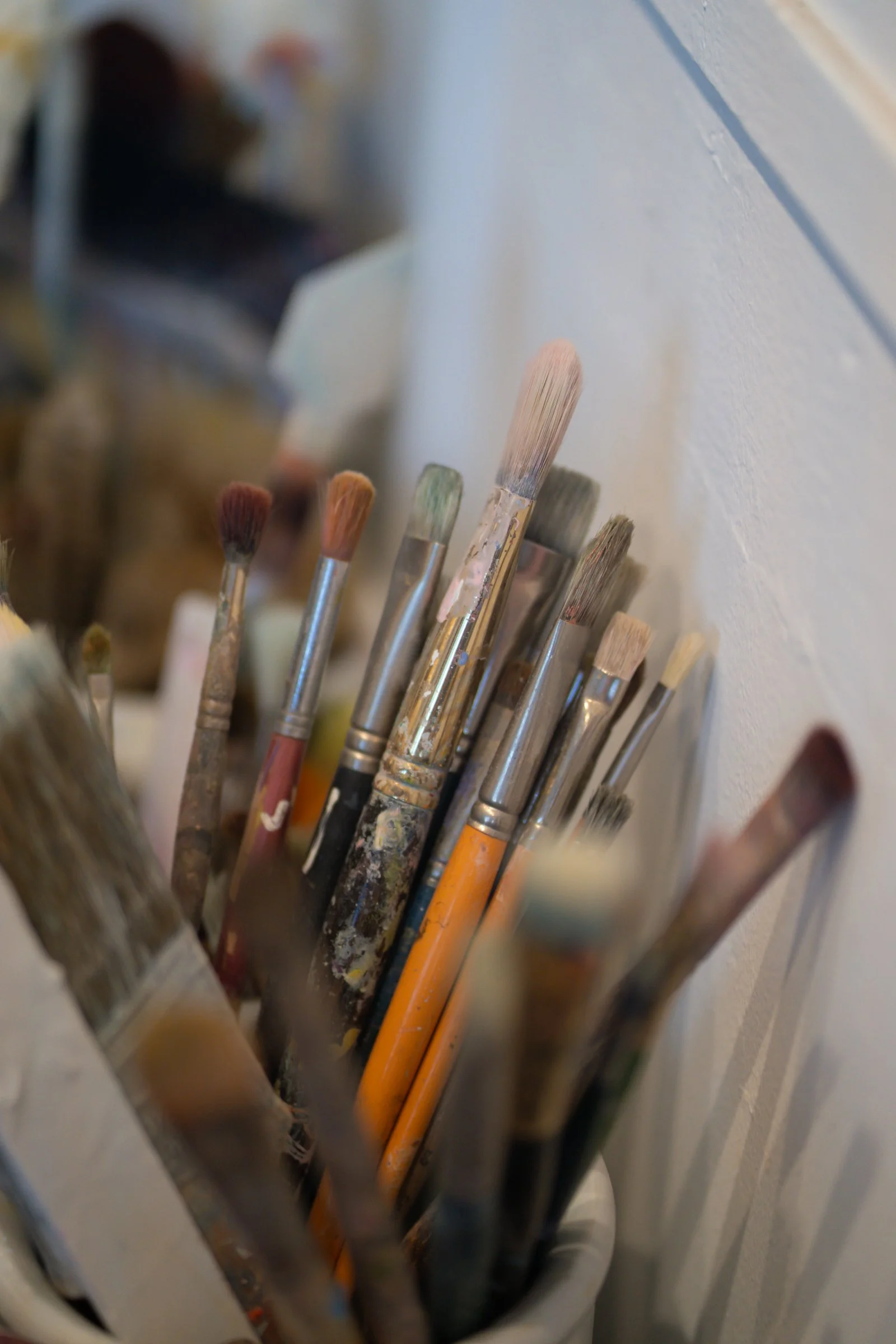 A collection of used paintbrushes with various sizes and bristle types in a container against a white wall.