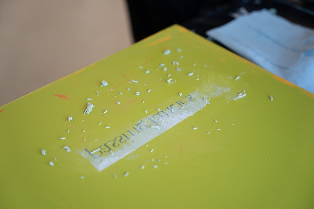 A bright yellow book with a strip of clear tape across the middle, on which small pieces of white tape are stuck, resting on a black surface with a gray object nearby.