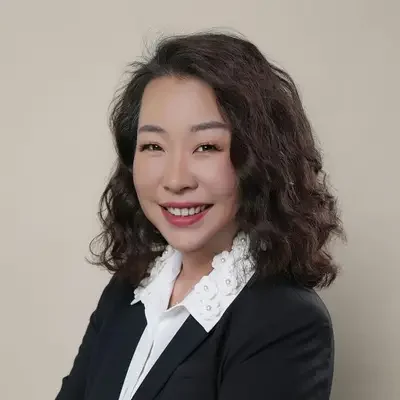 A woman with shoulder-length curly hair wearing a black blazer and white blouse, smiling at the camera.