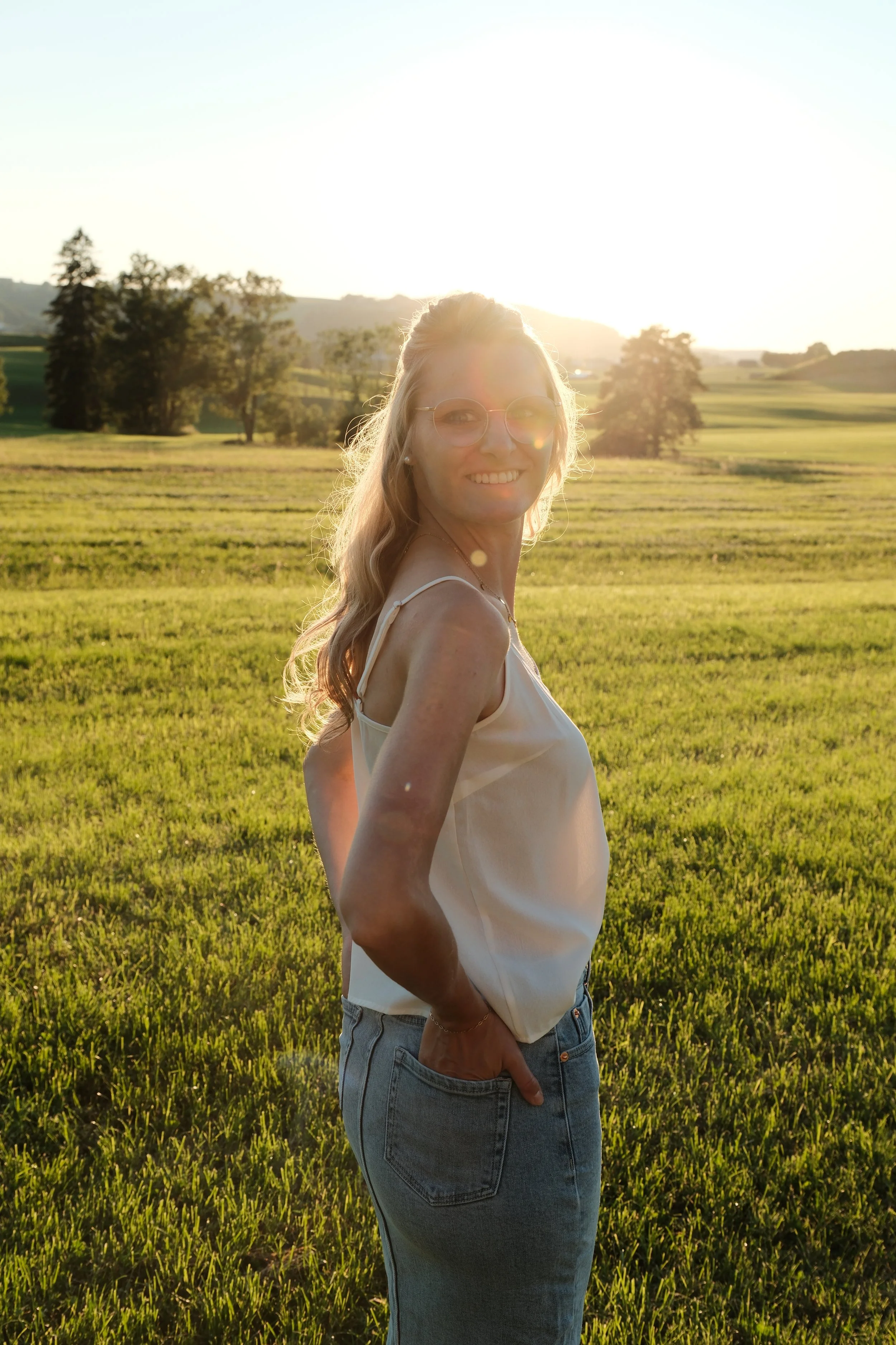 Lächelnde junge Frau im Sonnenuntergang in einer grünen Wiesenlandschaft