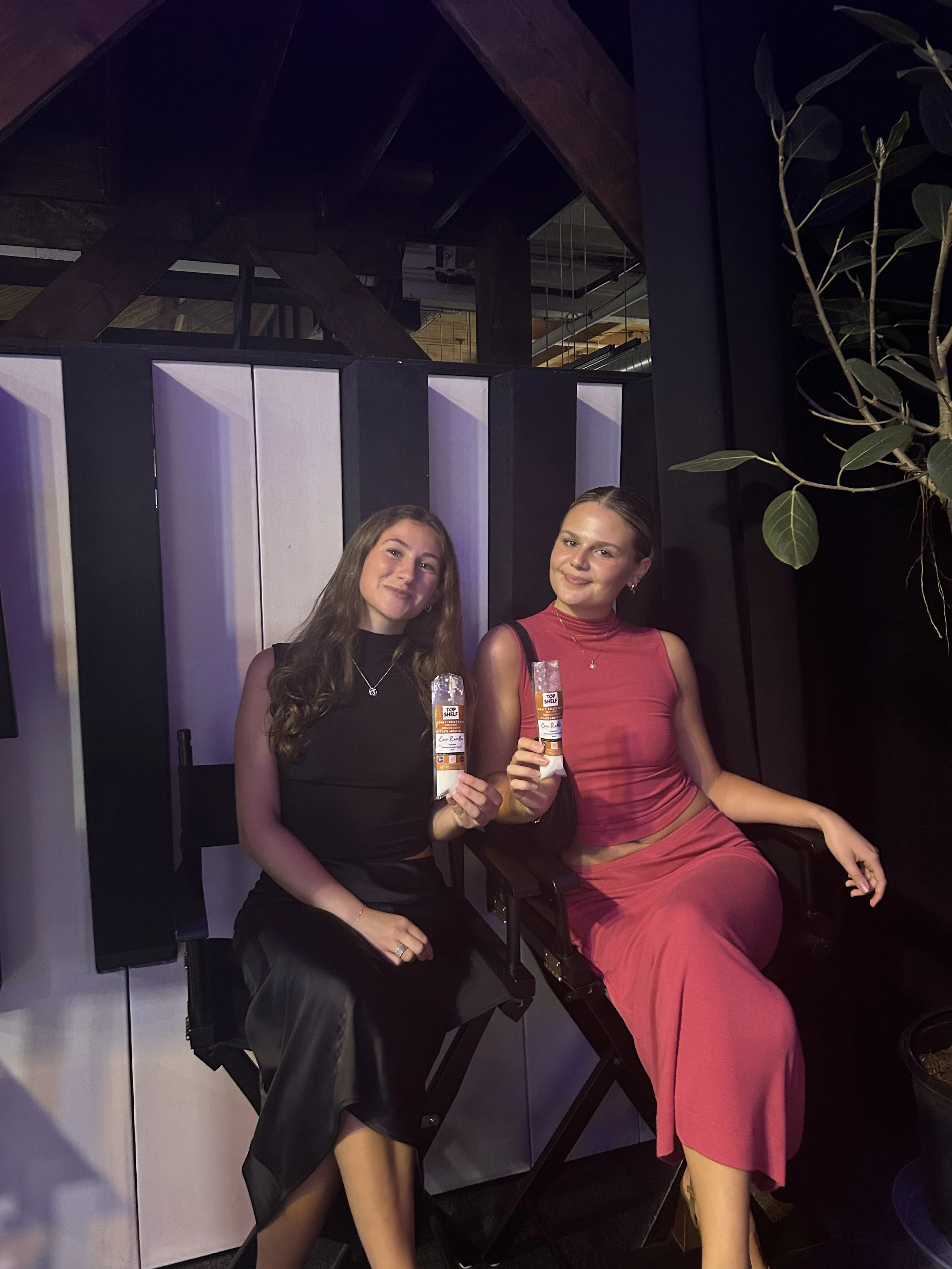 Two young women seated next to each other at an indoor event, holding raffle tickets and smiling at the camera.