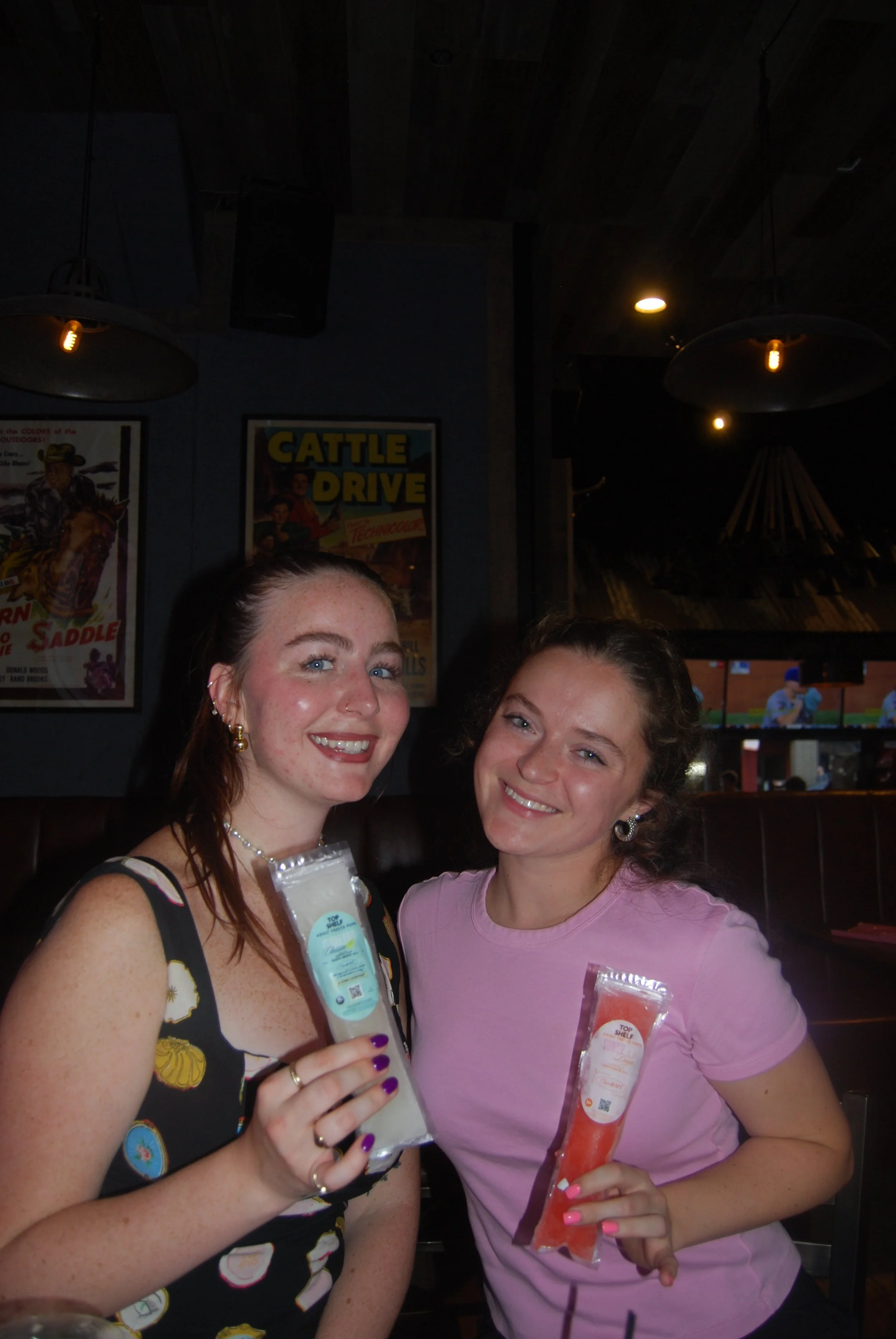 Two women smiling and holding packets of sauce in a restaurant.