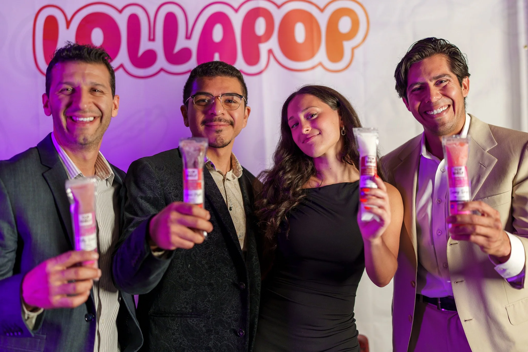 Four people smiling and holding tubes of glitter at a celebration with a sign that says 'GALLAPOP' in the background.