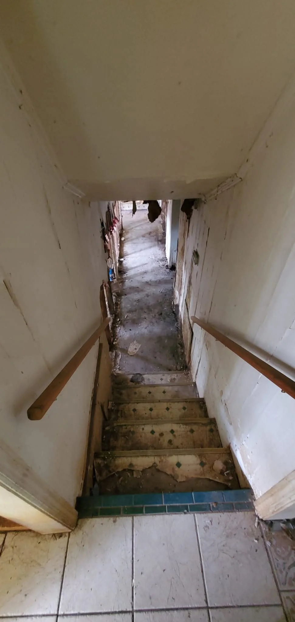 View of a worn-down staircase leading to a dilapidated hallway with cracked walls and debris on the floor.