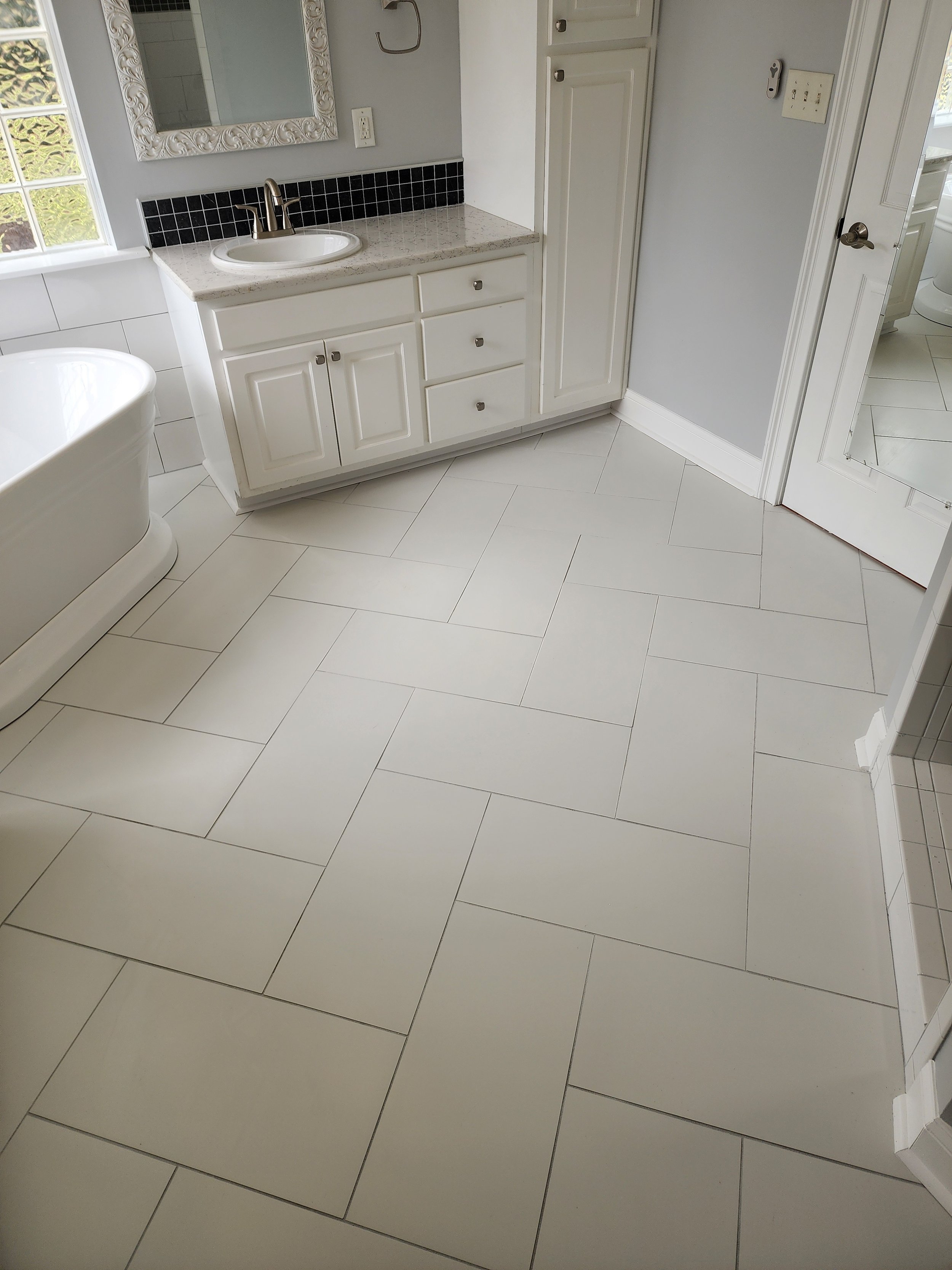 A bathroom with a white bathtub, a white vanity with a sink, a mirror, and tiled flooring.