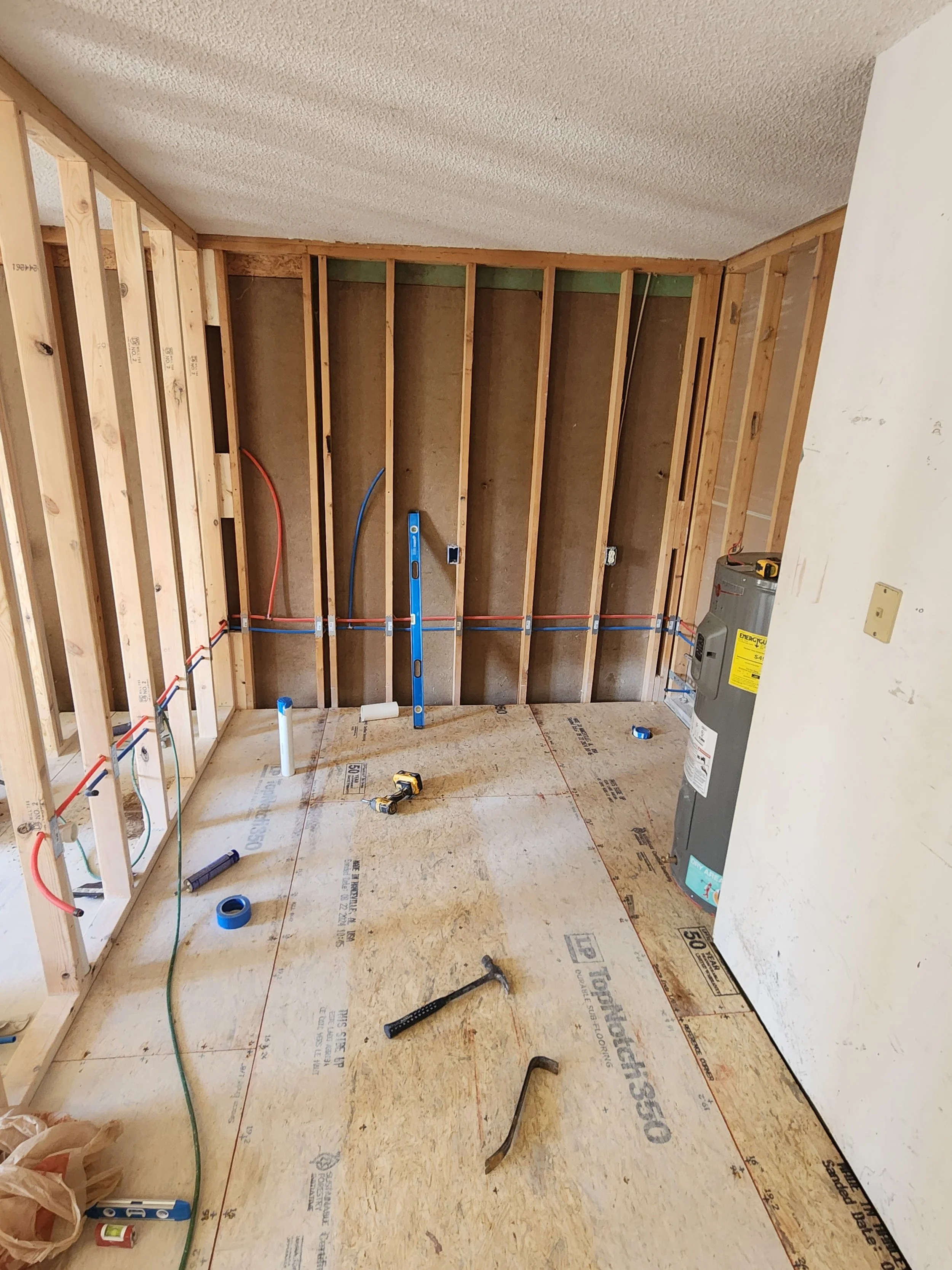 Interior of a room under construction with exposed wooden framing, electrical wiring, and construction tools on the floor.