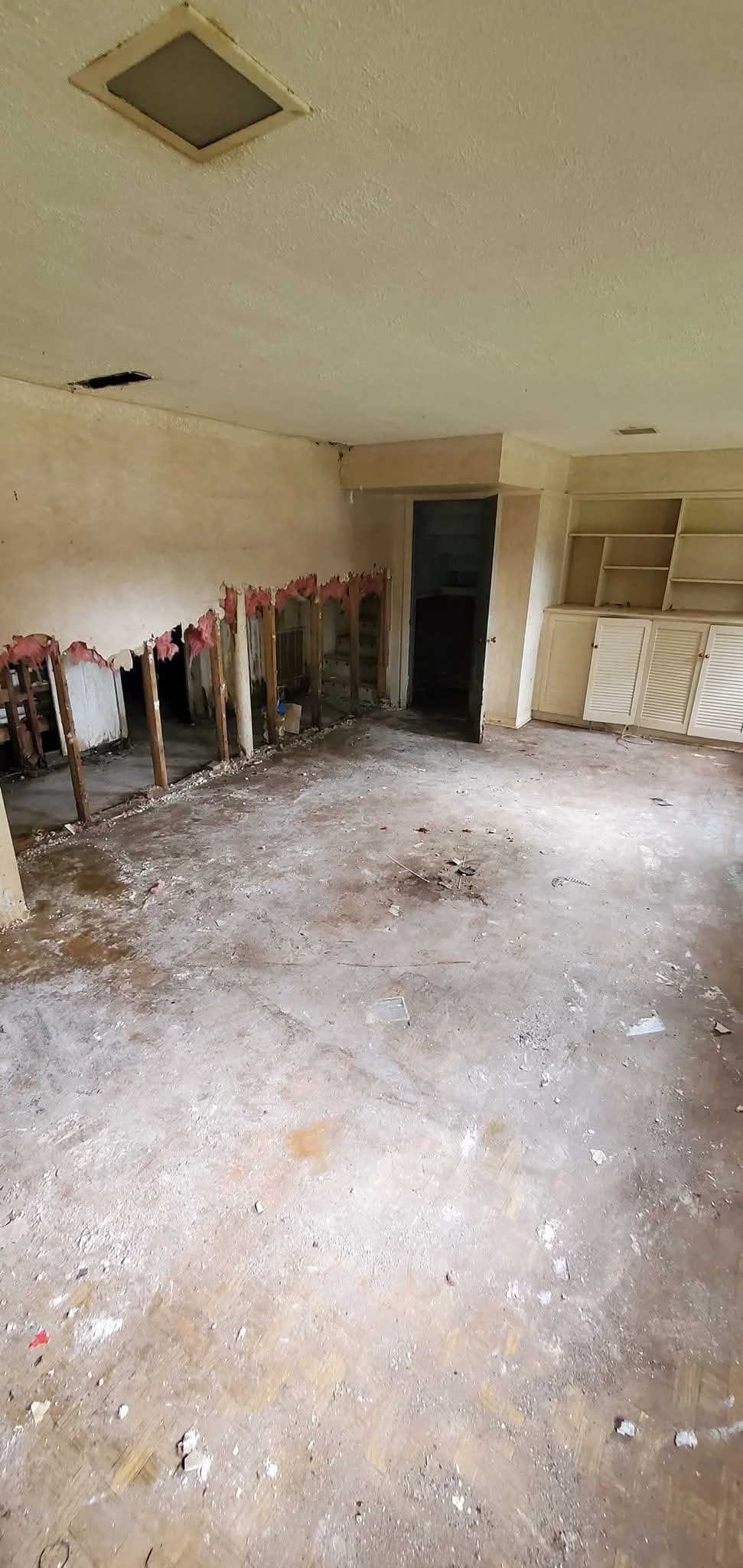 Room with demolished section showing exposed wall studs, open doorway, and built-in cabinetry.