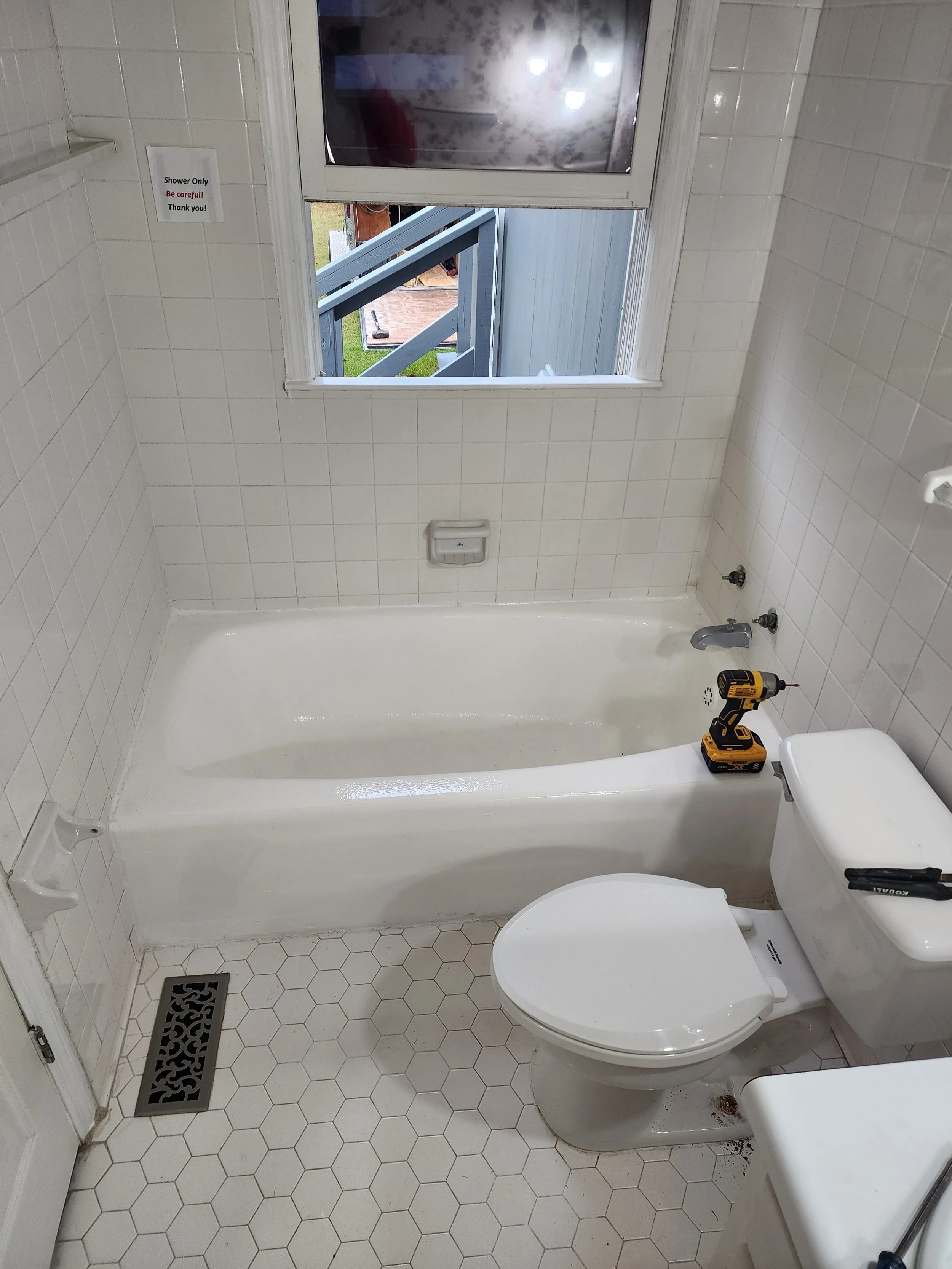 Bathroom with a bathtub, toilet, and a window, with a drill and screwdriver placed on the toilet tank, and a small sign on the wall indicating shower only.