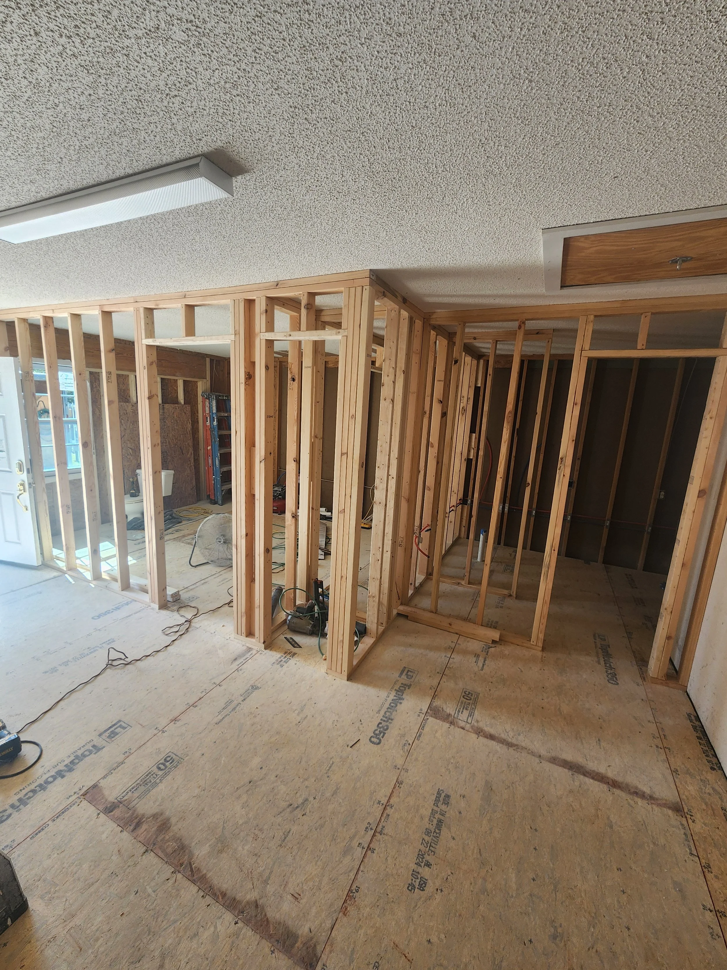 Interior view of a house under construction, showing wooden framing for walls and ceiling, construction tools, and electrical wiring.