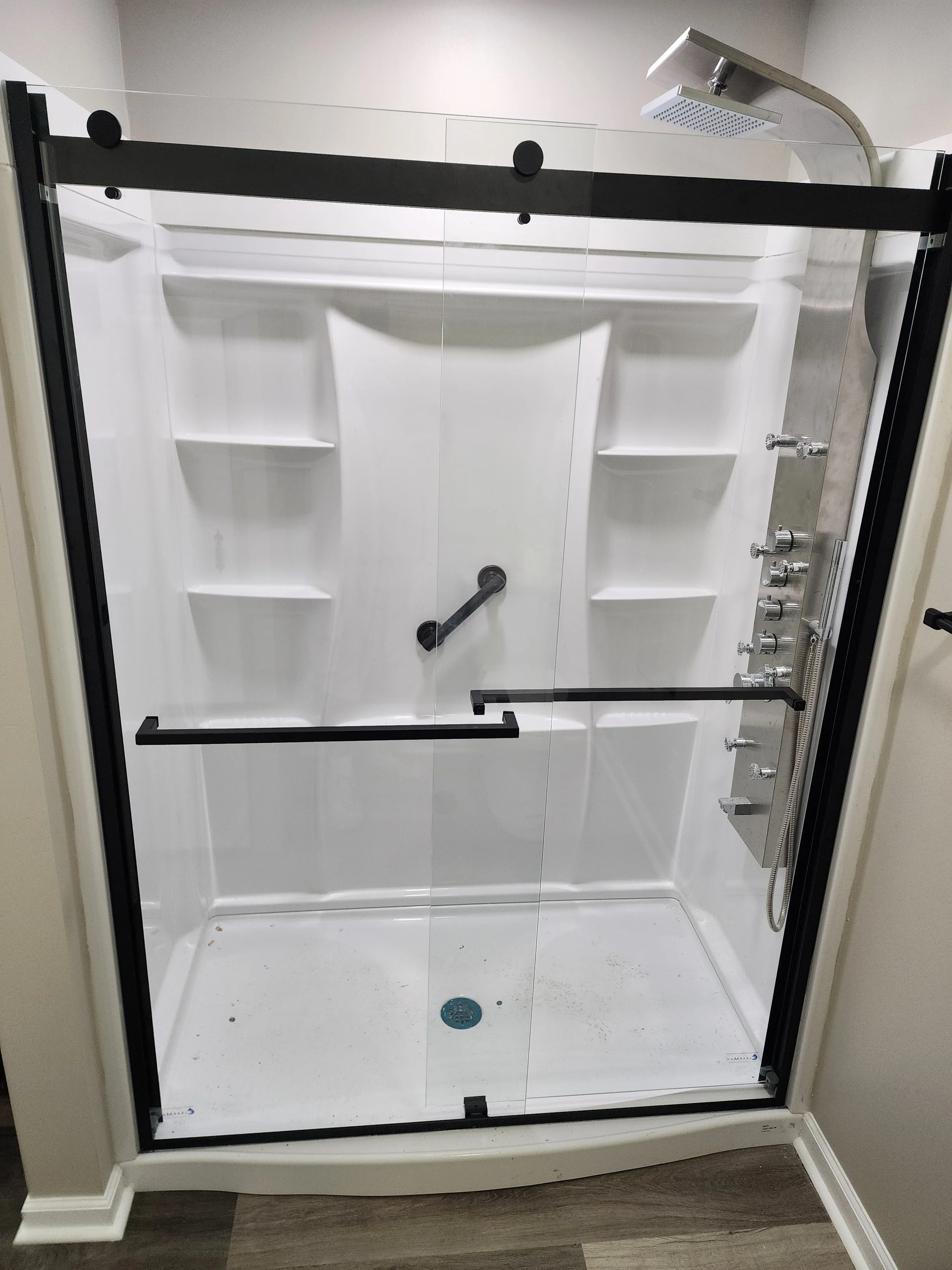 Empty walk-in shower with glass doors, built-in shelves, a rainfall showerhead, and control knobs.