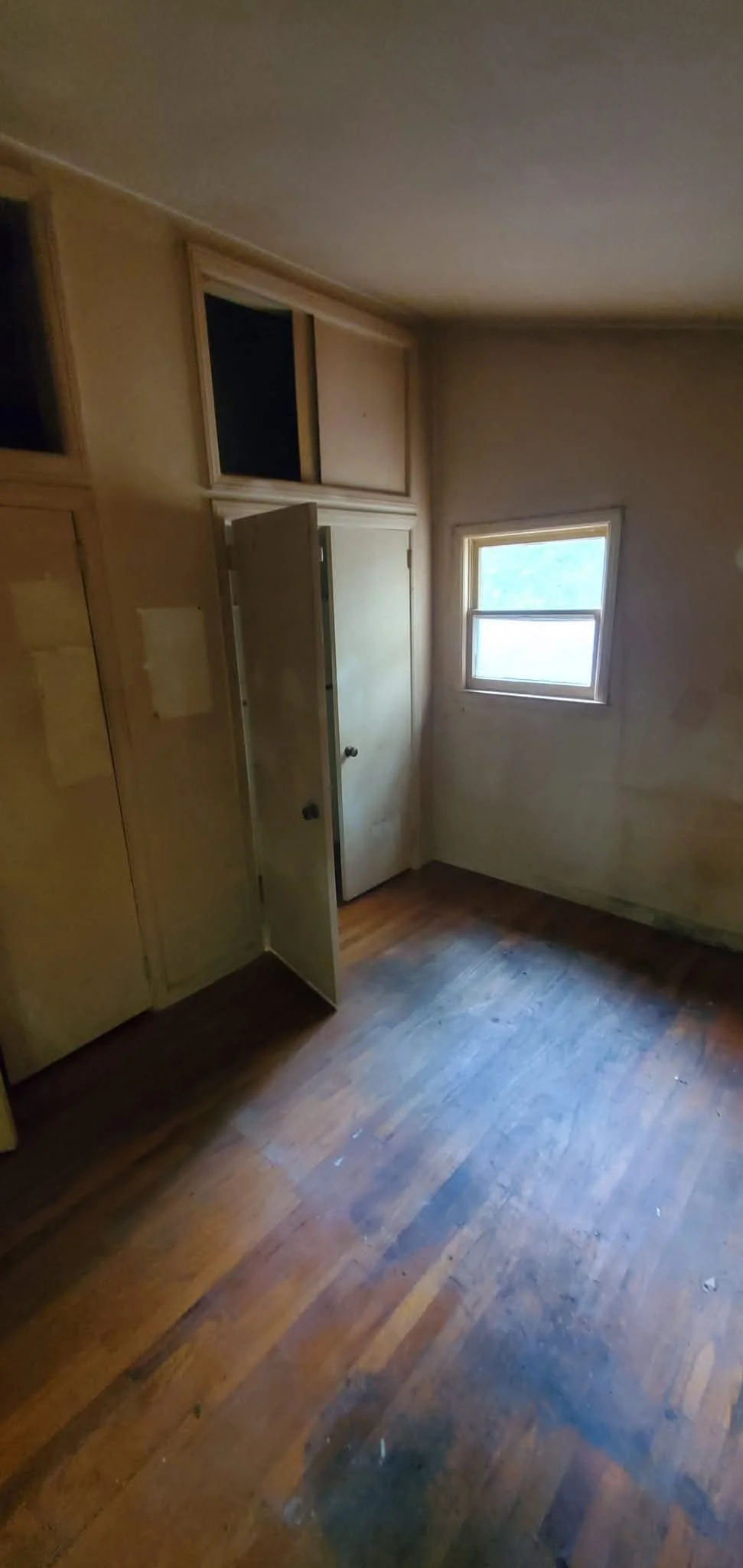 An empty, small room with a hardwood floor, a window, and a closet with open doors.