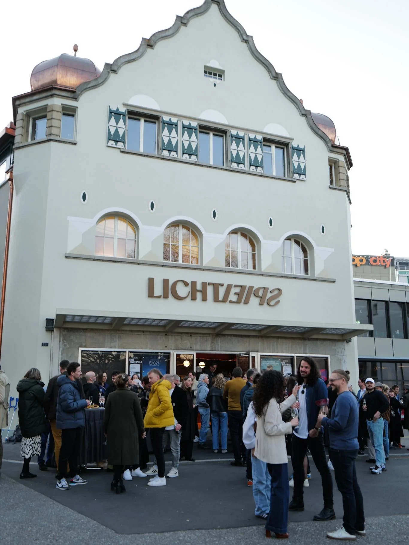 Eine Menschenmenge steht vor einem Gebäude mit der Aufschrift 'SPIELTHEATER'.