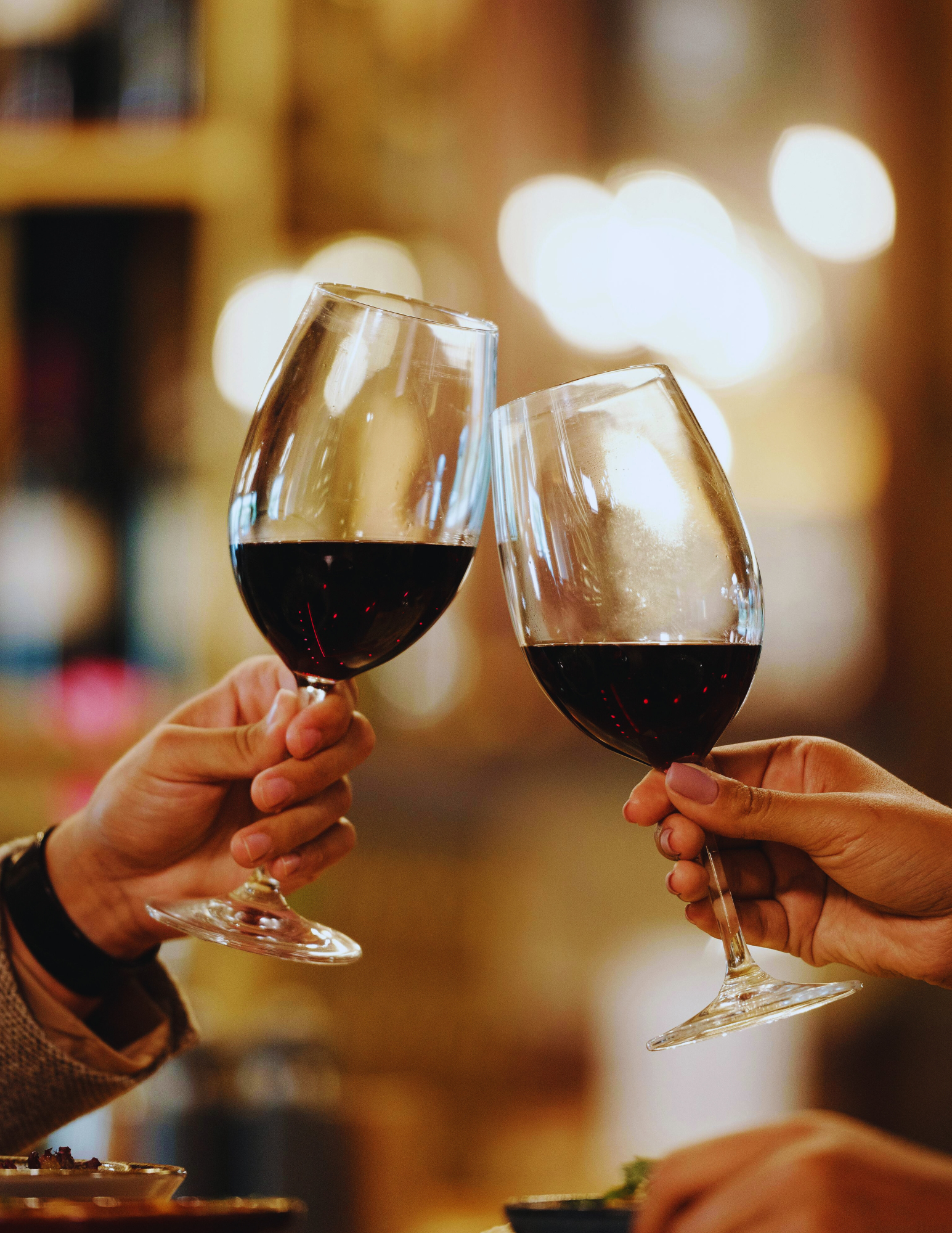 A woman with dark, shoulder-length hair sitting on a bench with a beige cushion, writing in a notebook. She is wearing a sleeveless beige top and tan pants. Behind her, there is a wooden panel wall and a framed abstract painting leaning against the wall, featuring brown and beige shapes. Sunlight creates shadows on the wall.