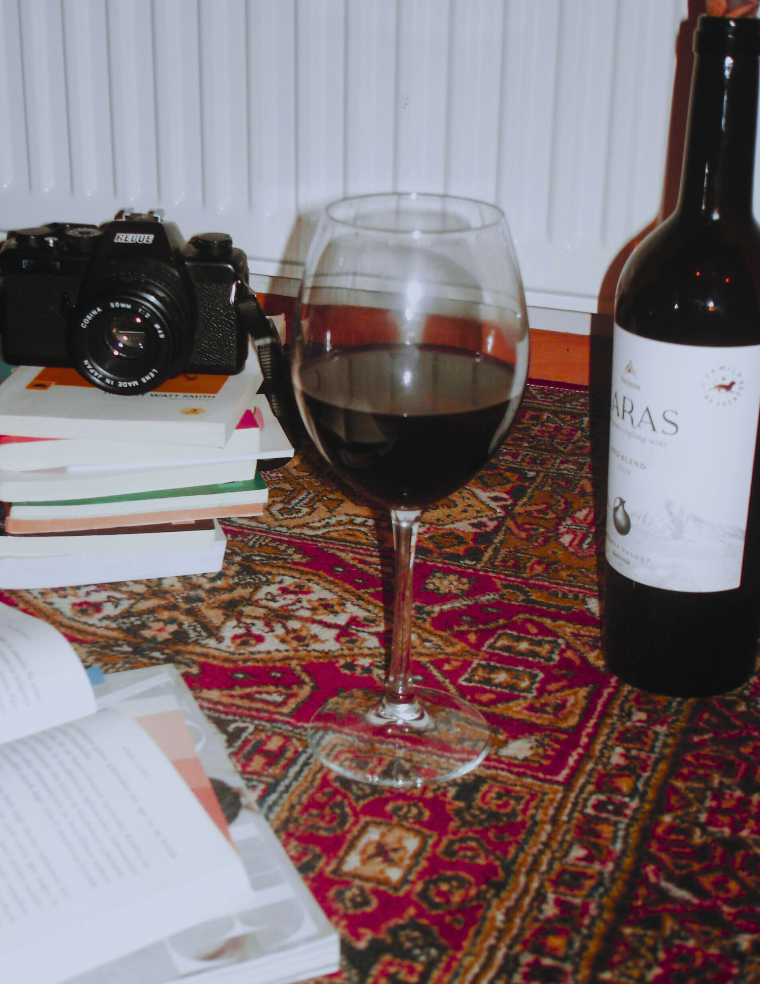 Young man sitting on a bench against a plain wall, wearing a grey polo shirt and cream-colored pants, looking to the side with a contemplative expression.