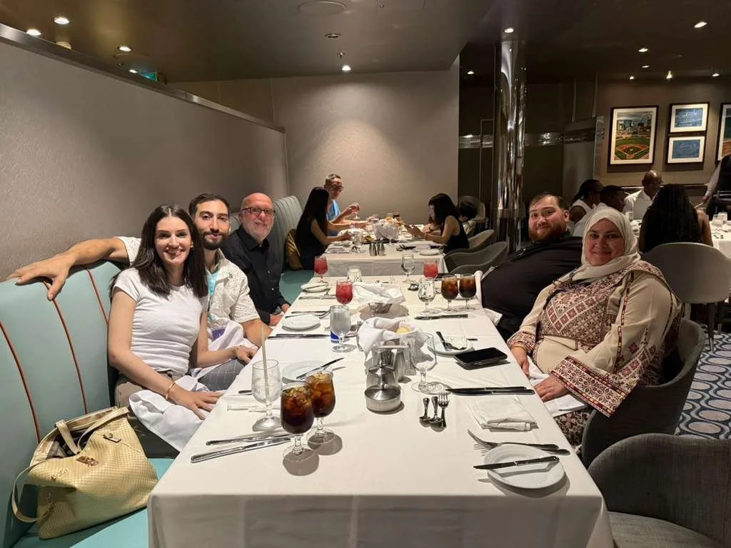 People sitting at a banquet table in a restaurant with drinks and plates, some engaged in conversation.