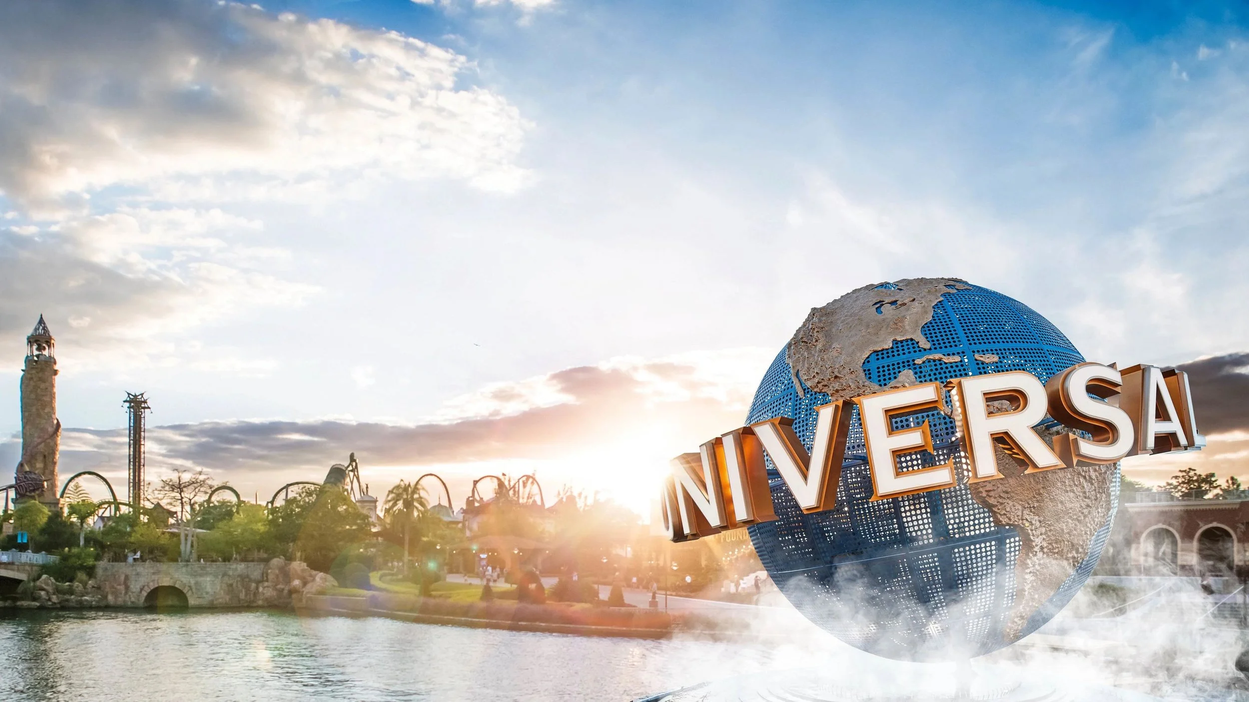 Universal Studios globe logo with the cityscape and amusement rides in the background at sunset.