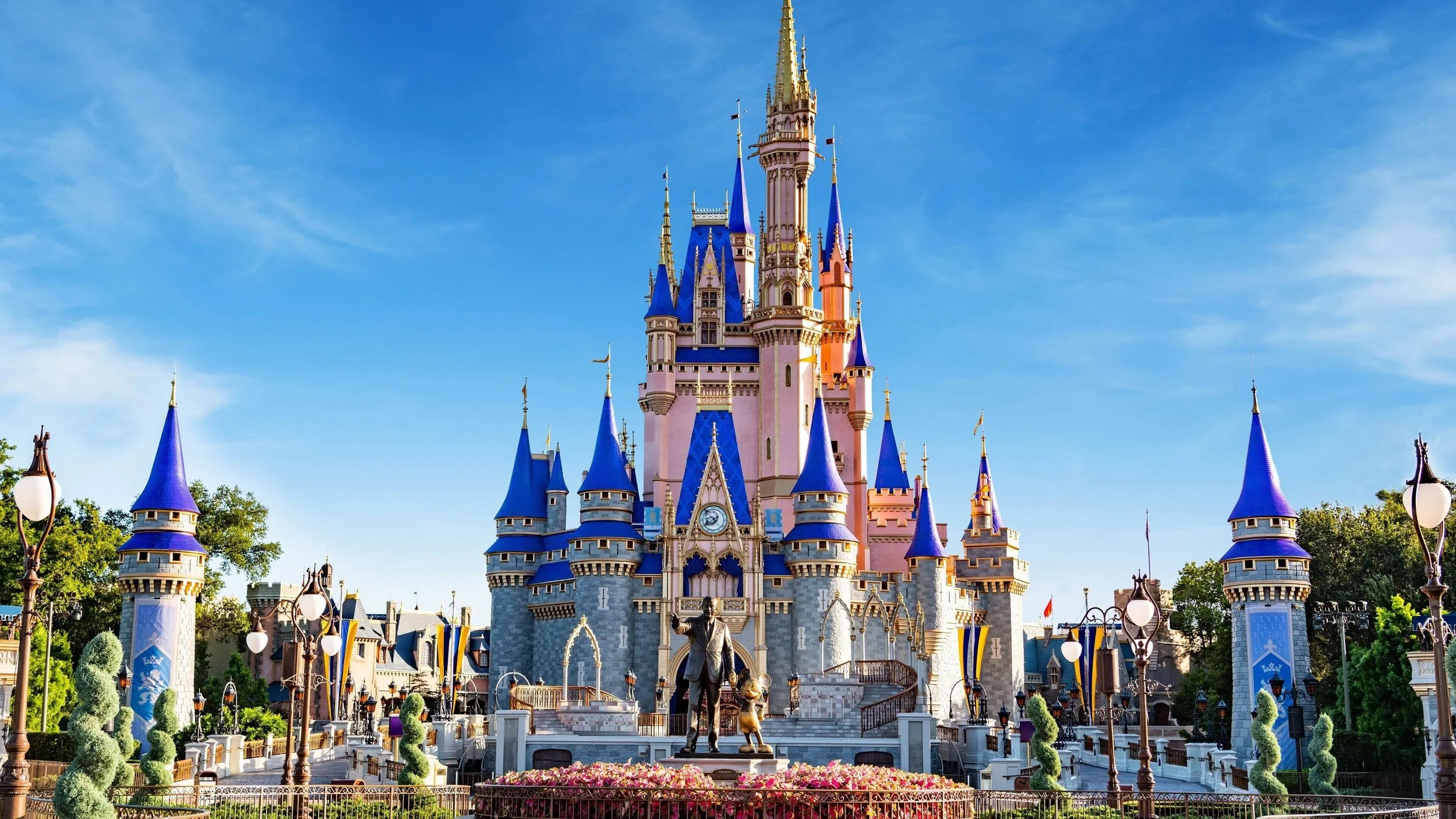 Pink castle with blue roofs at Disney theme park under a blue sky with few clouds.