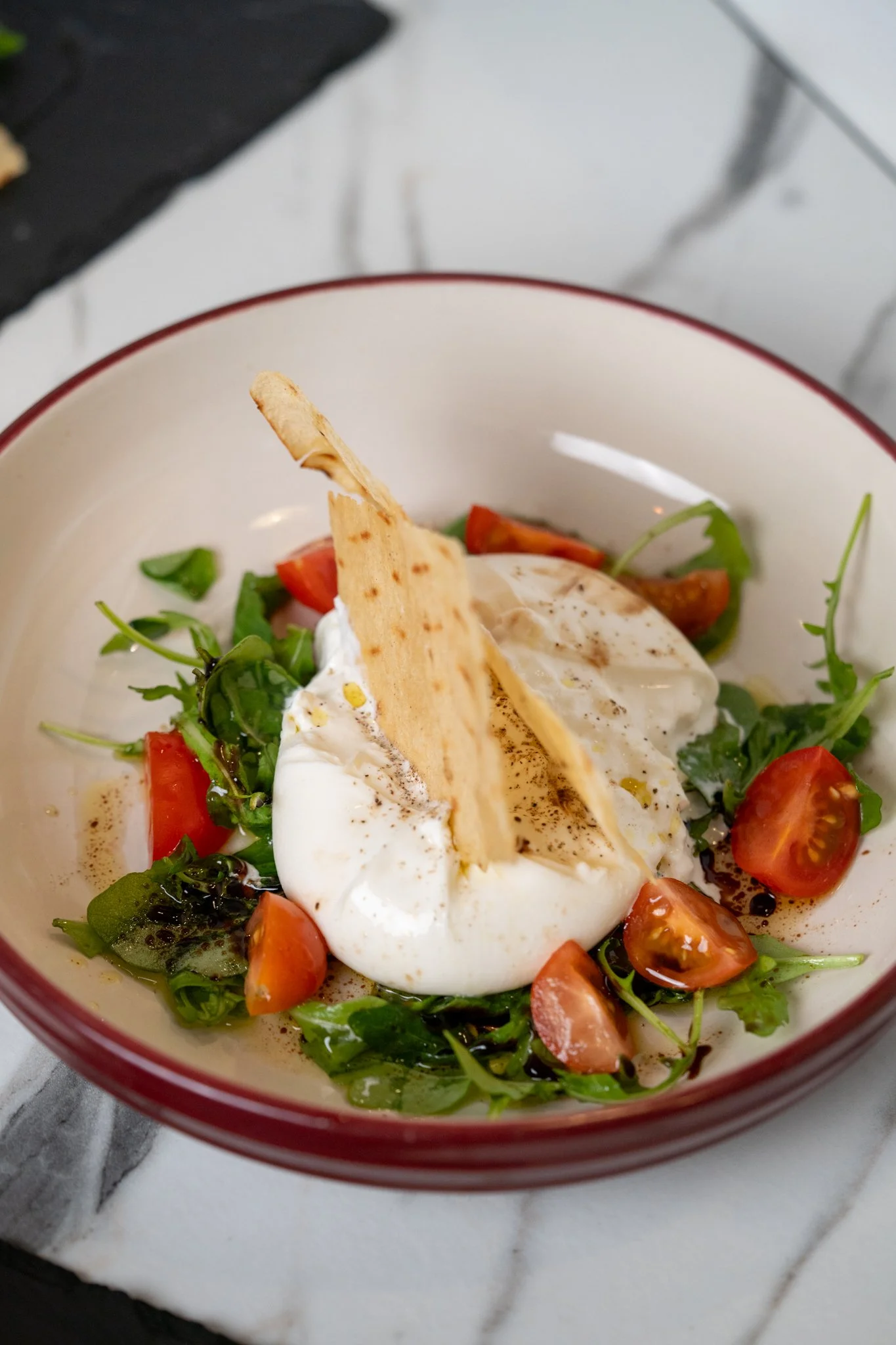 A bowl of fresh salad with cherry tomatoes, greens, poached eggs, and crispy bread slices on top, drizzled with dressing.
