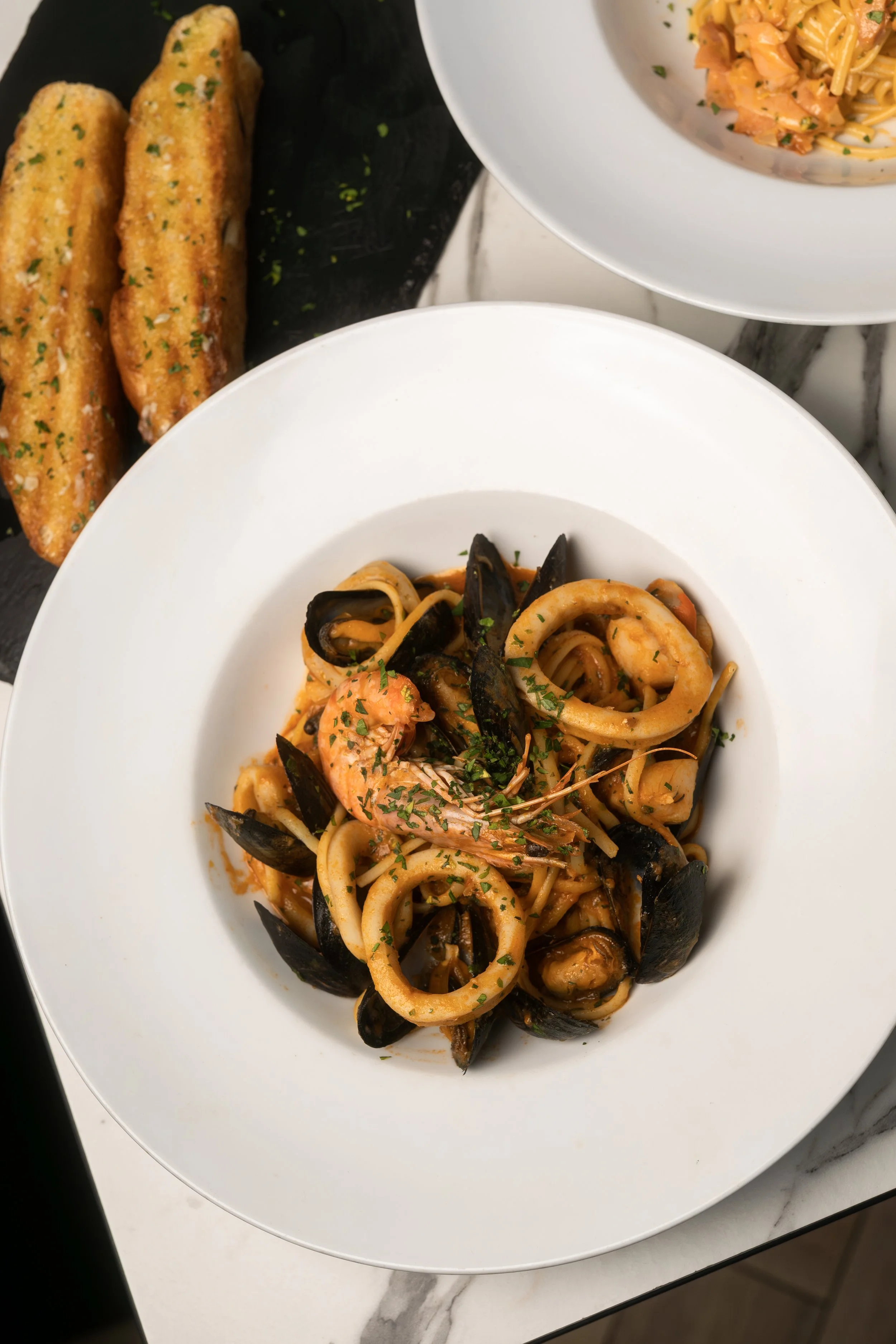 Seafood pasta with shrimp, mussels, and calamari in a tomato sauce, garnished with chopped parsley, served on a white plate