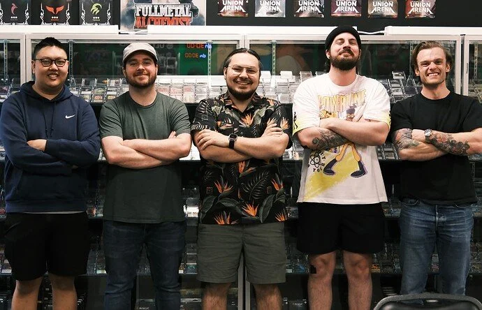 Five men standing side by side with arms crossed in front of a display of video games in a store.