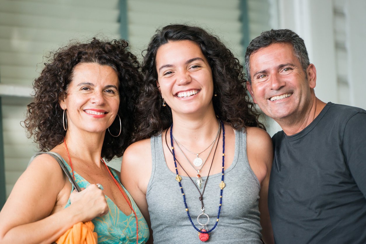 Three smiling people, two women and one man, standing close together outdoors.