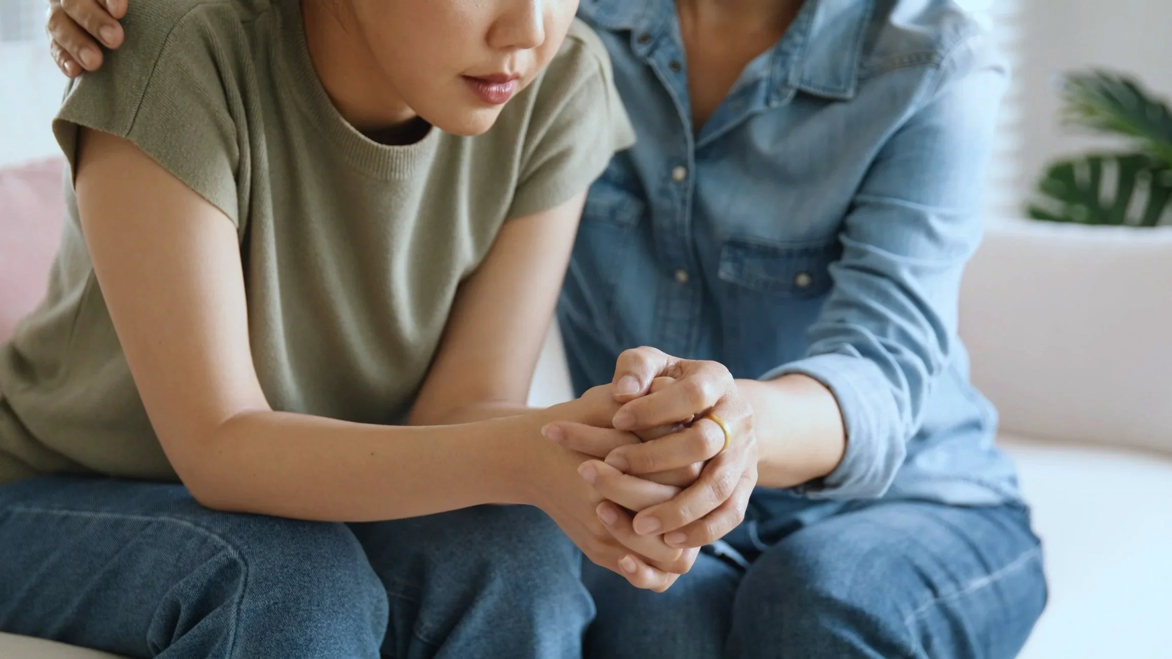 A woman in a green t-shirt and a man in a denim shirt sitting close together, holding hands with the woman's face showing a serious or emotional expression.