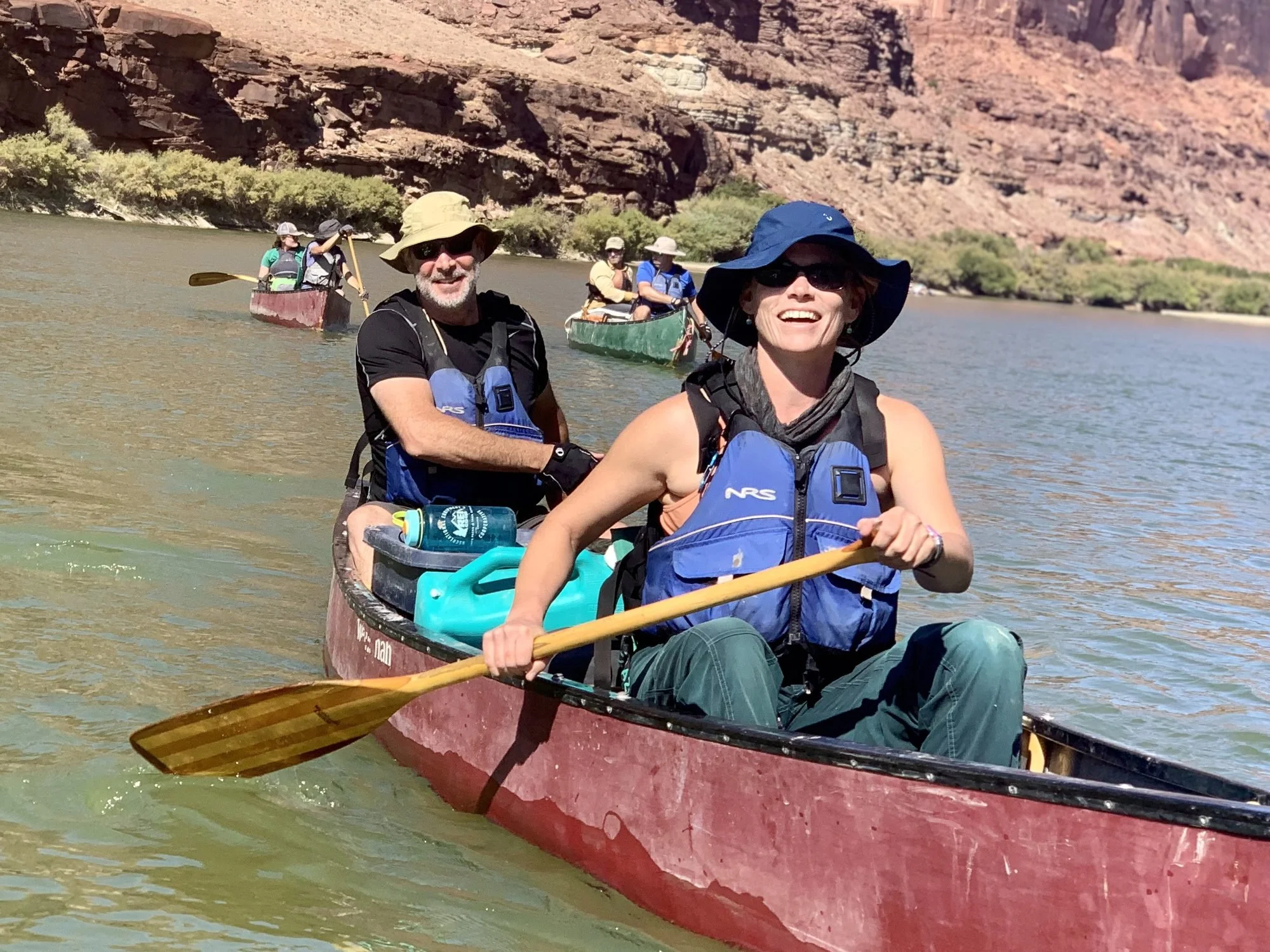 Group of people canoeing on a river with rocky desert landscape in the background