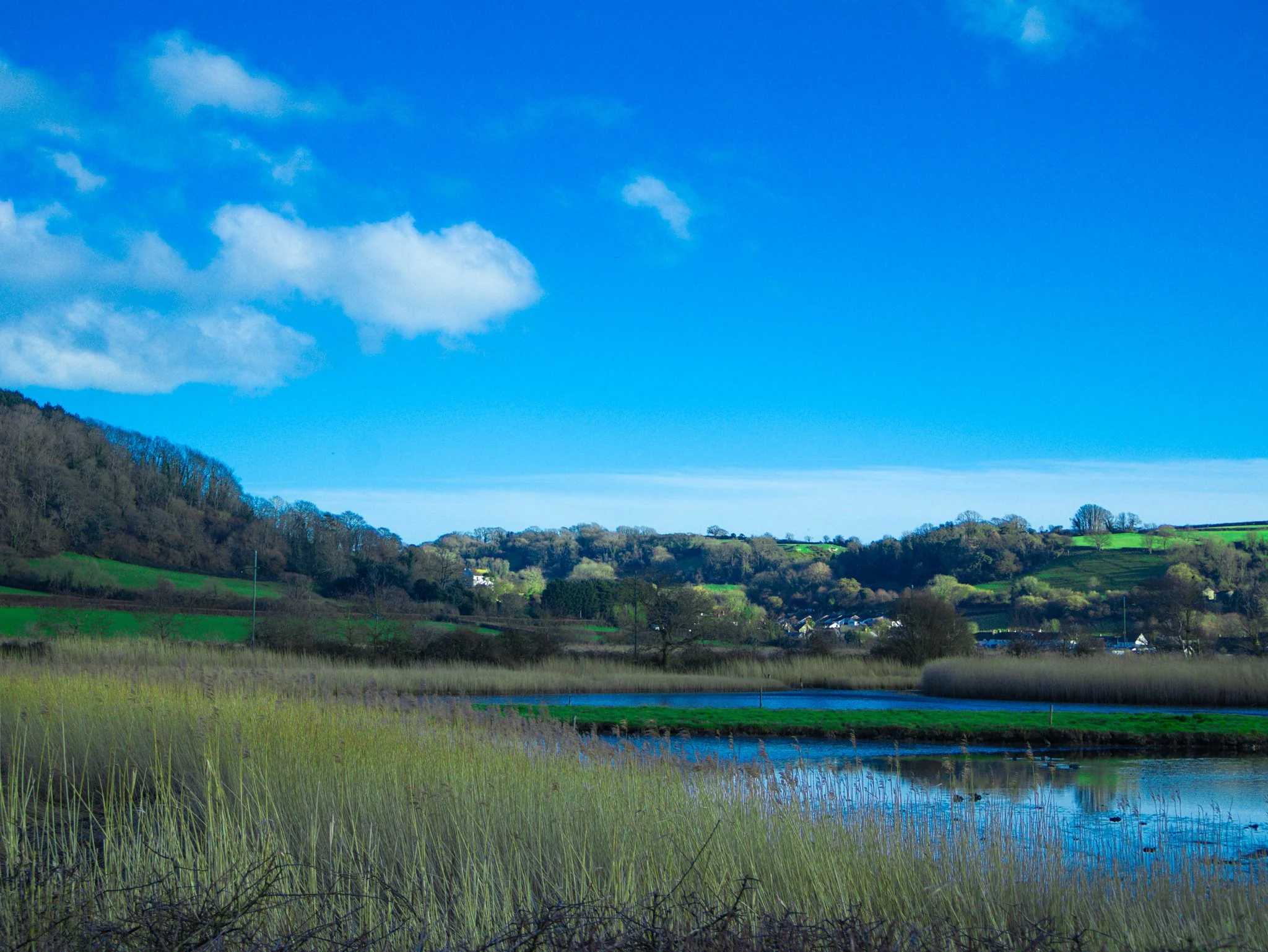 Scenic landscape with green hills, a blue sky with clouds, and a body of water in the foreground.
