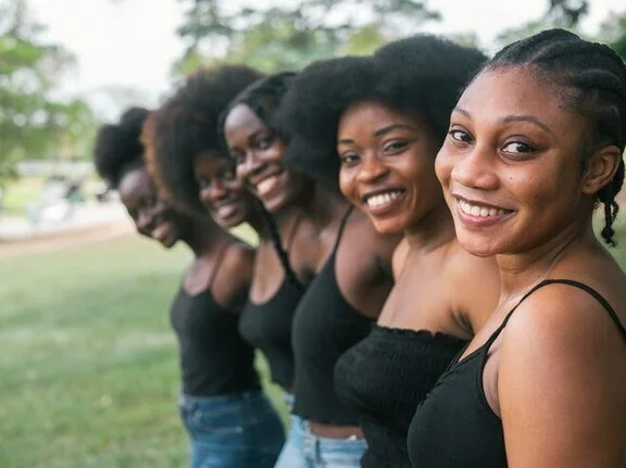 Five smiling women standing in a line outdoors on a grassy field, posing for a photo.