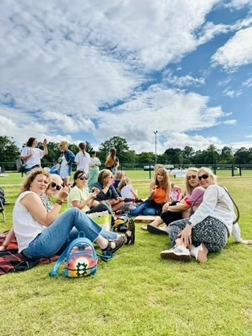 Outdoor fitness in Cranleigh. Group of women and children sitting on the grass outdoors on a sunny day