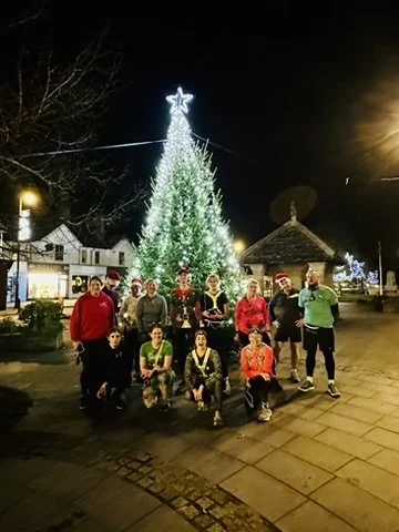 Outdoor fitness in Cranleigh. Group of people posing in front of a lit Christmas tree and holiday decorations at night.