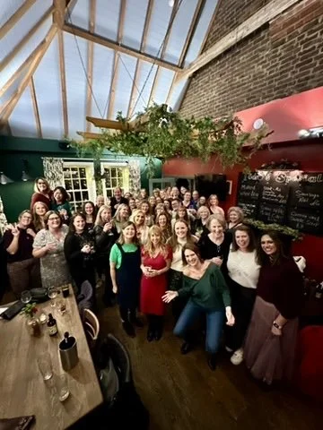 Outdoor fitness in Cranleigh. Group of people gathered in a cozy restaurant or cafe with high wooden ceilings and exposed brick walls, smiling for a group photo.
