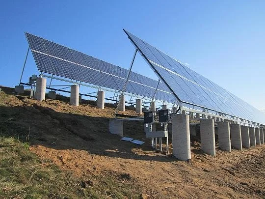 Solar panel installation on elevated supports on a hillside under a clear blue sky.
