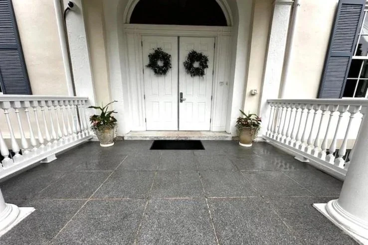 After power washing photo of Front porch with white double doors decorated with two holiday wreaths, flanked by potted plants, with blue shutters and white railings on each side.