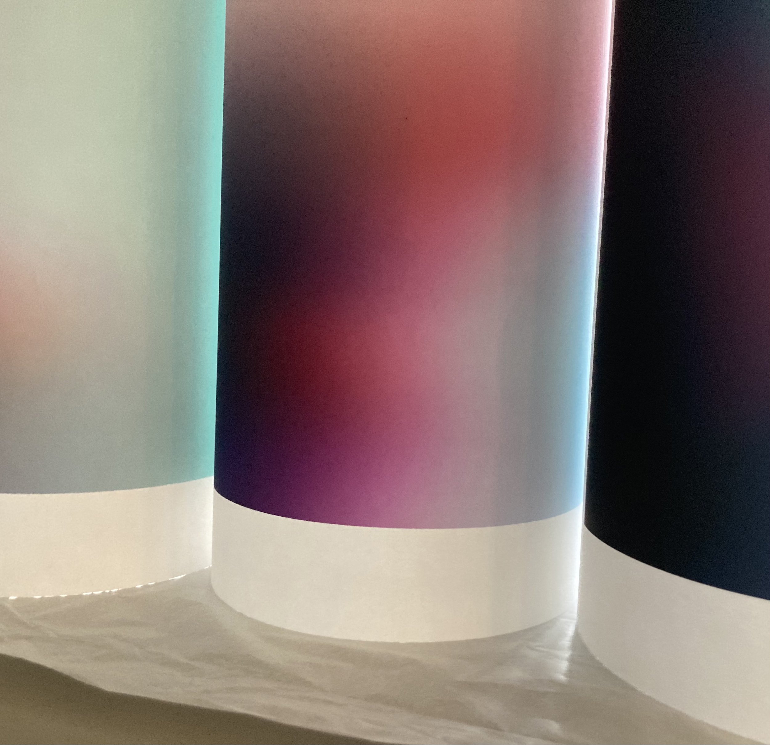 Close-up of a white surface with colorful semi-transparent curved panels, including green, purple, blue, and black, with reflections and shadows.