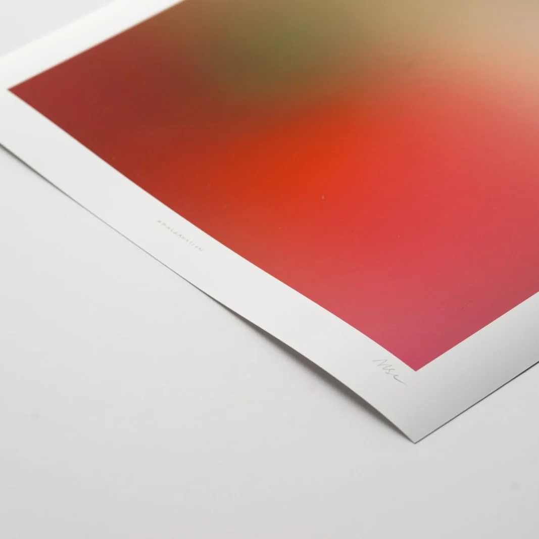 Close-up of a printed art piece with a gradient of colors from green to red, on white paper with a white border and faint handwritten markings.