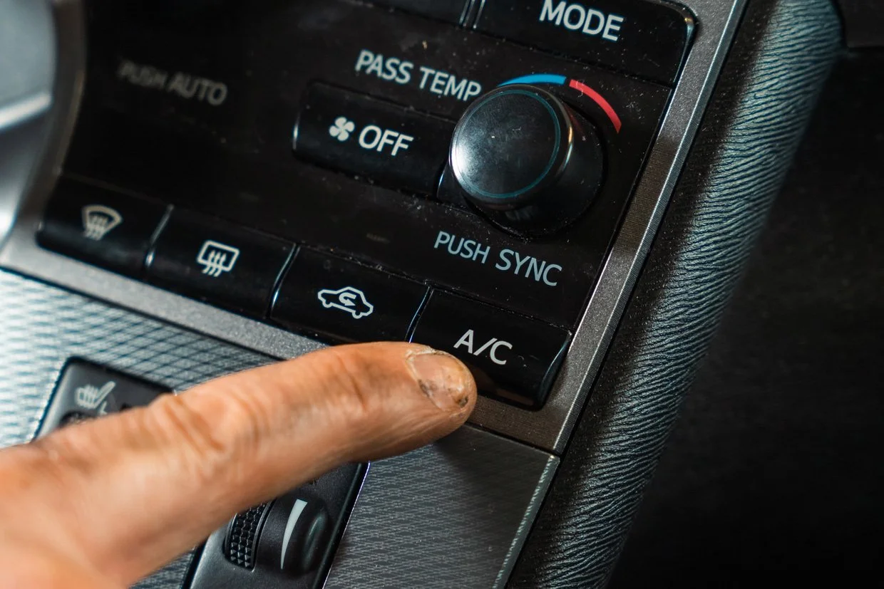 Close-up of a person's finger pressing the A/C button on a car's climate control panel.