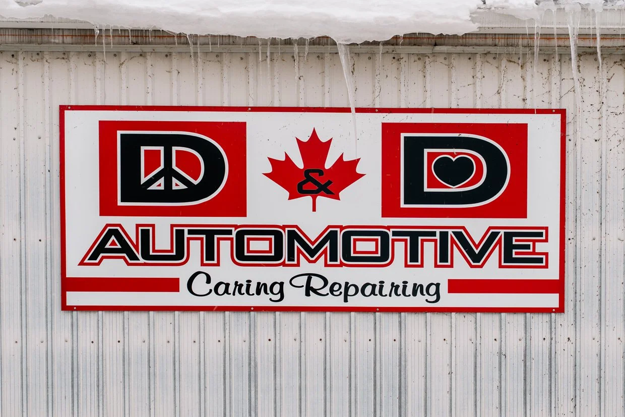 Sign for D&D Automotive Car Care Repair featuring red, black, and white colors with a peace sign, a maple leaf, and hearts.