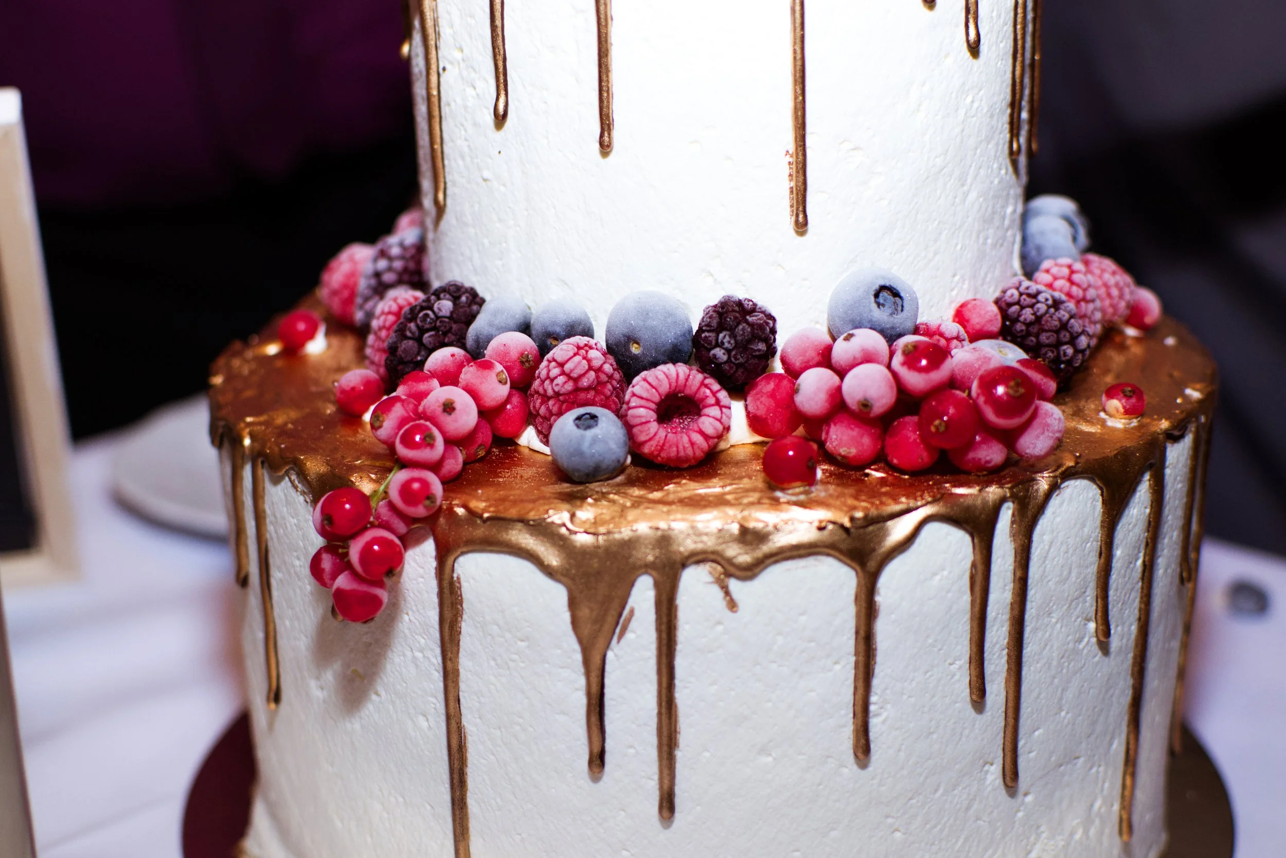 Zweistöckige Torte mit weißen Zuckerglasur und Schokoladenglasur, Dekoration mit Beeren und roten Johannisbeeren.