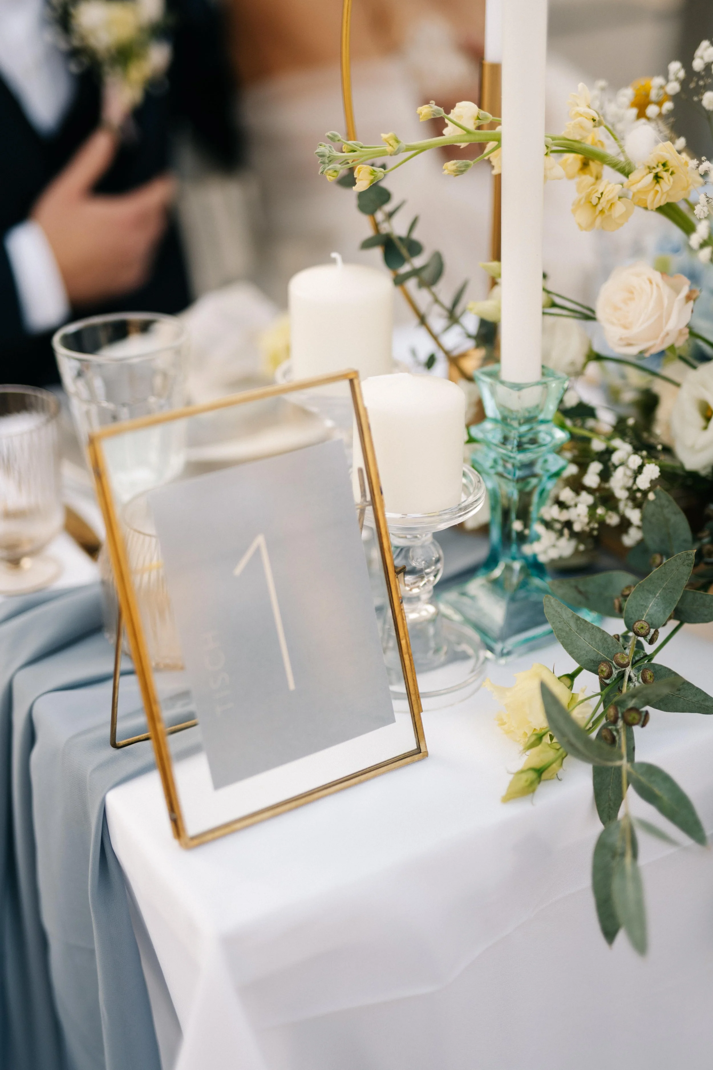 Tischdekoration mit weißen Kerzen, Blumen und einer Platznummer 1 bei einer Hochzeit oder Feier.