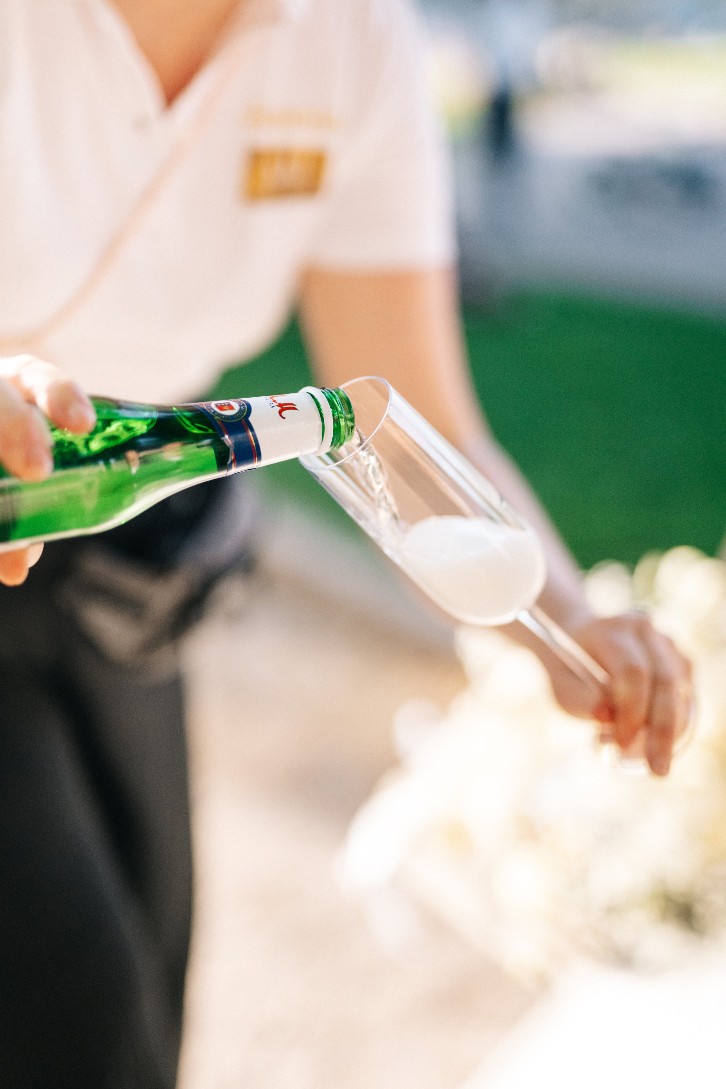 Eine Person gießt ein Getränk aus einer grünen Flasche in ein Champagnerglas.