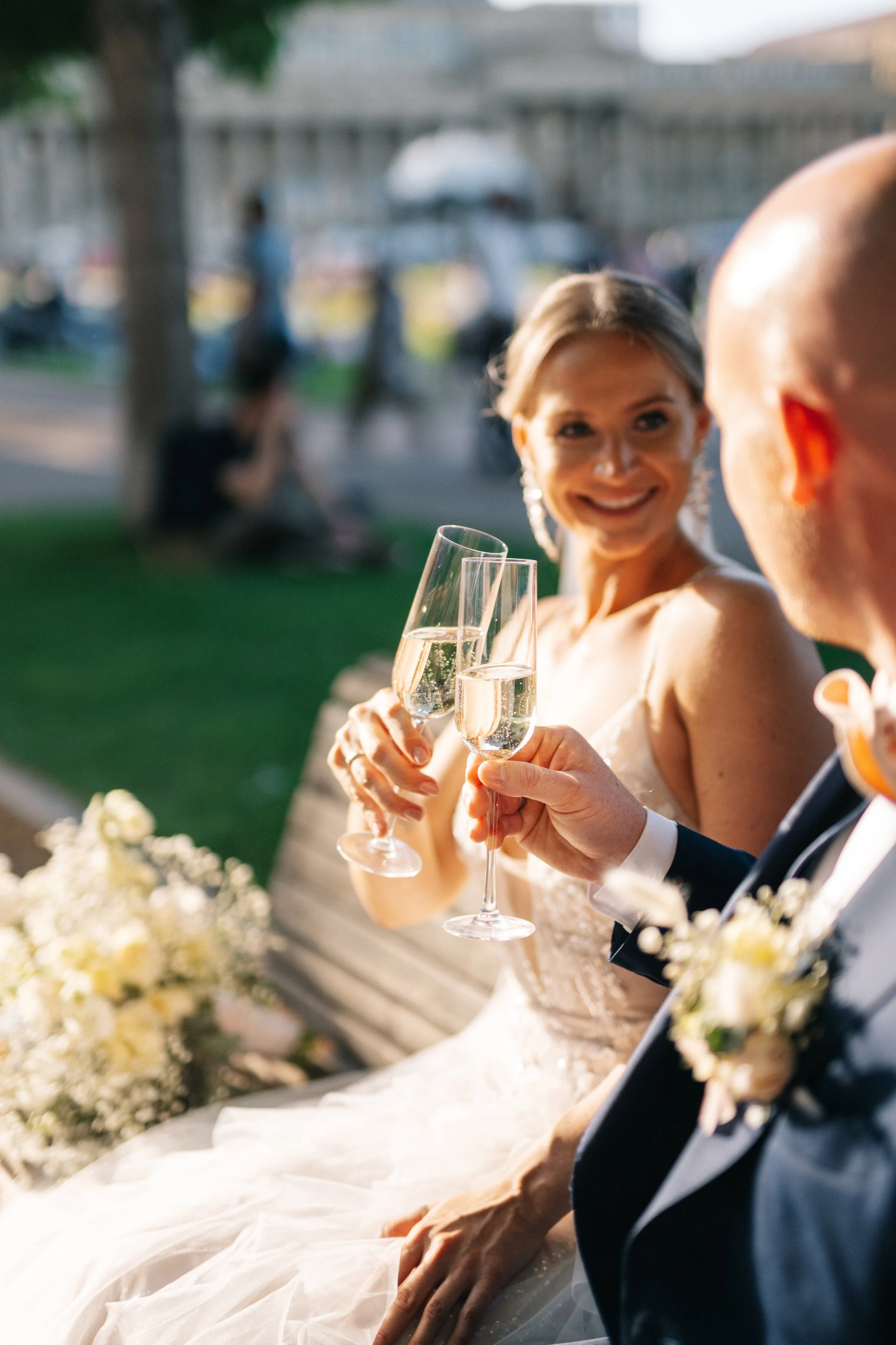 Ein Brautpaar stößt mit Champagner an, bei ihrer Hochzeit im Freien, während Sonnenlicht auf sie scheint.