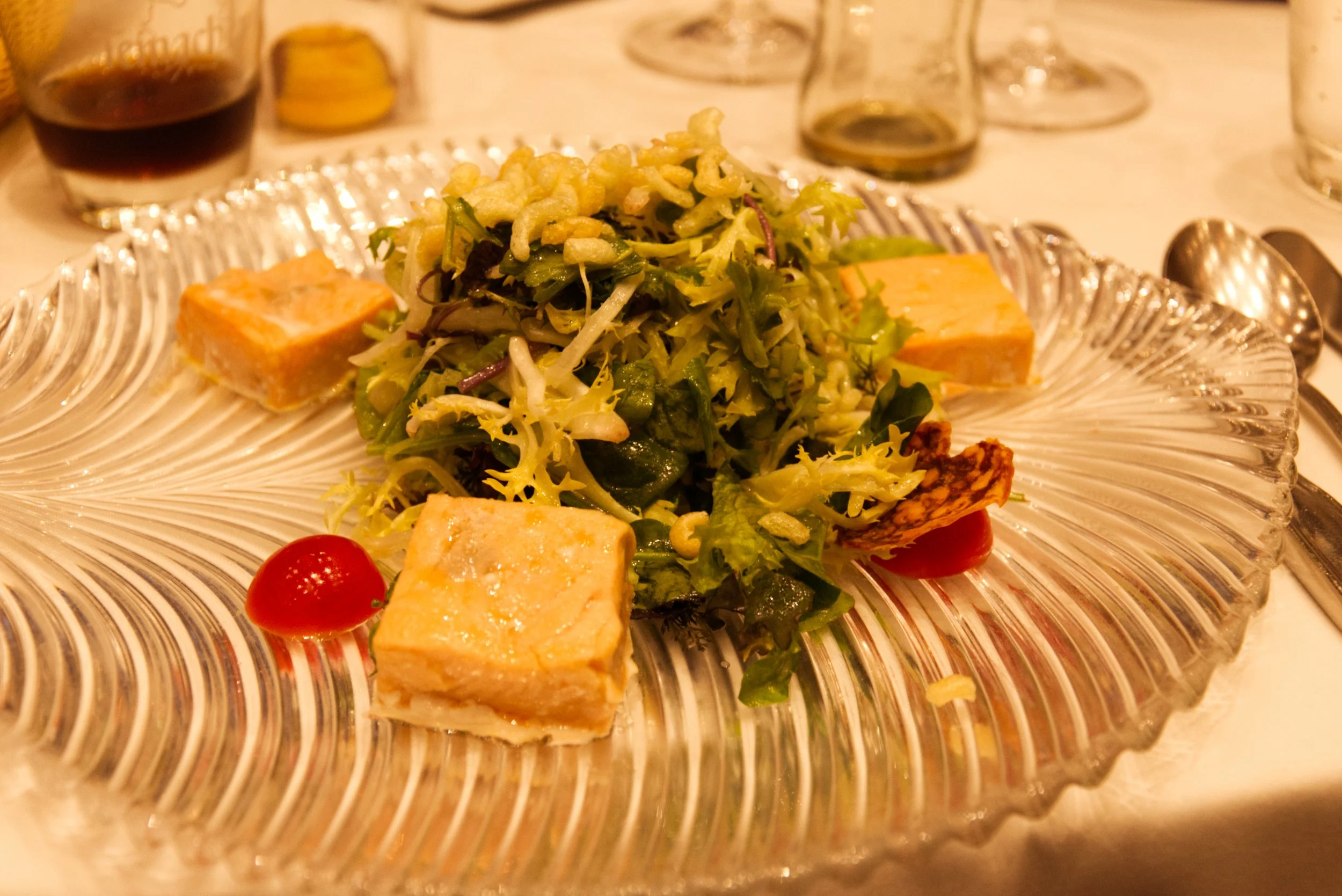 Gemischter grüner Salat mit Tomaten, Croutons, Käsewürfeln und dicken Plastiktorten auf einem Glasservice bei einer Mahlzeit.