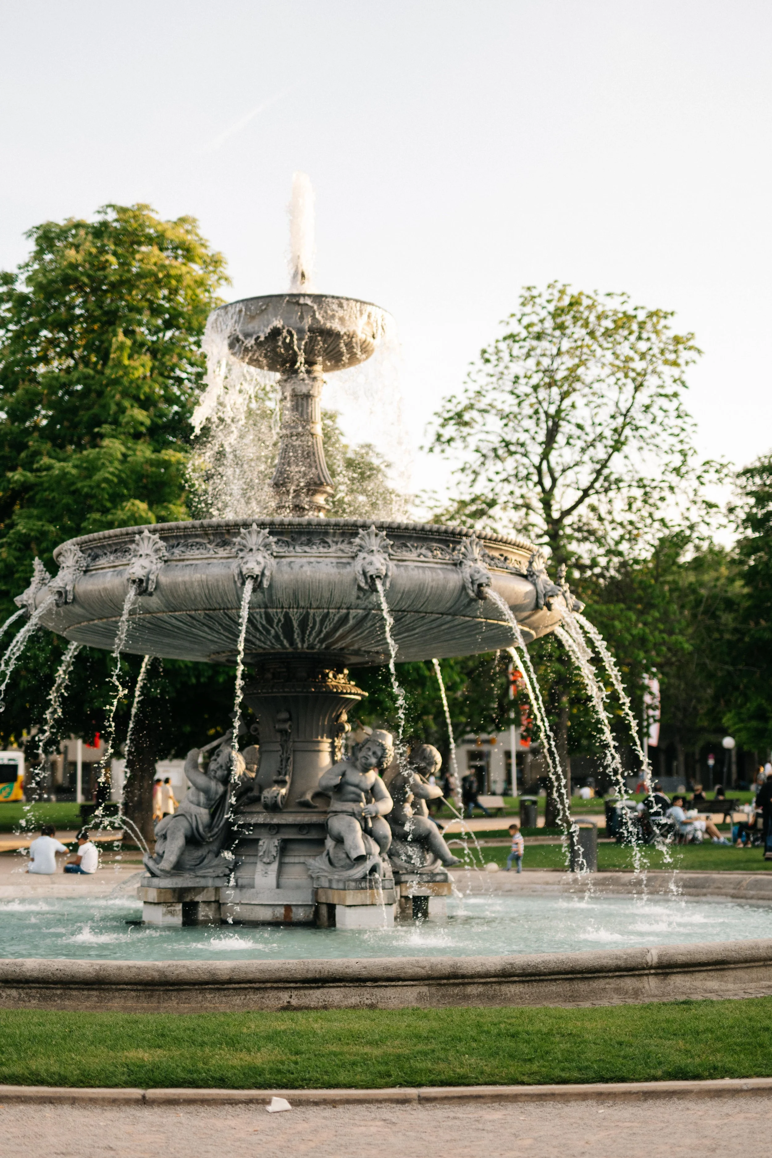 Brunnen mit Wasserfall und Skulpturen in öffentlichem Park bei Sonnenuntergang