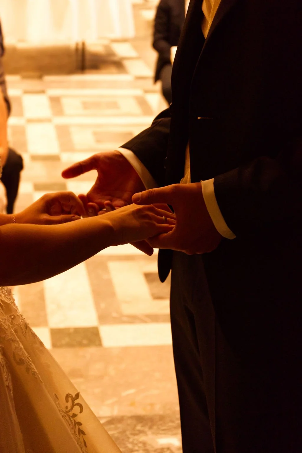 Ein Paar bei einer Eheschließung hält sich gegenseitig an den Händen fest, während ein Offiziant ihre Eheringe austauscht.