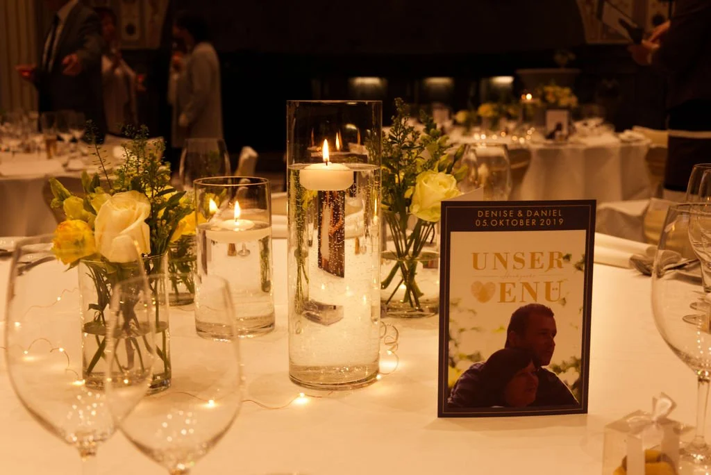 Ein festlich gedeckter Tisch mit Kerzen, Blumenarrangements und einem Menü-Schild bei einer Hochzeit am 5. Oktober 2019.